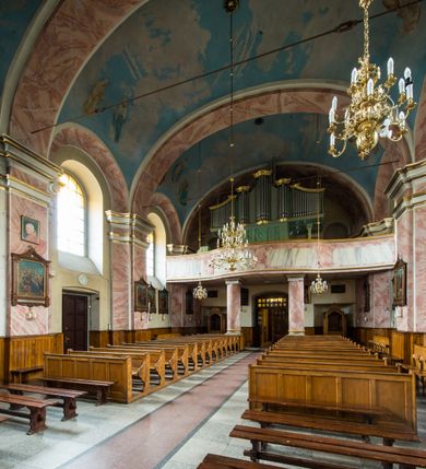 Zdjęcie nr 7: Murowany kościół otrzymał układ jednonawowej świątyni z węższym prezbiterium zwróconym ku północy i wieżą dostawioną do nawy od południa. Prezbiterium jest jednoprzęsłowe zakończone spłaszczoną apsydą. Na jego przedłużeniu usytuowano czworoboczną zakrystię. Prostokątna nawa jest trójprzęsłowa o zaokrąglonych narożnikach. Od frontu wzniesiono czworoboczną wieżę o ściętych narożnikach, flankowaną piętrowymi lokalnościami. Wysunięto ją lekko ku przodowi, gdzie przechodzi wklęsłymi płaszczyznami w boczne części fasady. Jej górne piętro nakryte cebulastym hełmem zostało opięte po bokach wolutami, obok których ustawiono kamienne klasycystyczne wazy. Elewacje zewnętrzne artykułowano podziałami ramowymi, zamykając wysokości ścian gzymsem gurtowy. Na końcu nawy na siodłowym dachu pokrytym blachą umieszczono czworoboczną wieżyczkę na sygnaturkę zwieńczoną cebulastym hełmem z krzyżem. Podobnym dachem nakryto prezbiterium. Wnętrze kościoła zostało rozczłonkowane lizenami z wklęsłymi półlizenami po bokach, ponad którymi rozciągnięto odcinki belkowania. Całość nakryto sklepieniem żaglastym na zdwojonych gurtach. Od południa w nawie urządzono chór muzyczny wsparty na dwóch kolumnach z parapetem wklęsłowypukłym. W prezbiterium usytuowano ołtarz główny, a w nawie dwa ołtarze boczne. Tu także na ścianie zachodniej zawieszono ambonę.  