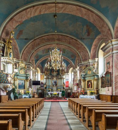 Zdjęcie nr 13: Murowany kościół otrzymał układ jednonawowej świątyni z węższym prezbiterium zwróconym ku północy i wieżą dostawioną do nawy od południa. Prezbiterium jest jednoprzęsłowe zakończone spłaszczoną apsydą. Na jego przedłużeniu usytuowano czworoboczną zakrystię. Prostokątna nawa jest trójprzęsłowa o zaokrąglonych narożnikach. Od frontu wzniesiono czworoboczną wieżę o ściętych narożnikach, flankowaną piętrowymi lokalnościami. Wysunięto ją lekko ku przodowi, gdzie przechodzi wklęsłymi płaszczyznami w boczne części fasady. Jej górne piętro nakryte cebulastym hełmem zostało opięte po bokach wolutami, obok których ustawiono kamienne klasycystyczne wazy. Elewacje zewnętrzne artykułowano podziałami ramowymi, zamykając wysokości ścian gzymsem gurtowy. Na końcu nawy na siodłowym dachu pokrytym blachą umieszczono czworoboczną wieżyczkę na sygnaturkę zwieńczoną cebulastym hełmem z krzyżem. Podobnym dachem nakryto prezbiterium. Wnętrze kościoła zostało rozczłonkowane lizenami z wklęsłymi półlizenami po bokach, ponad którymi rozciągnięto odcinki belkowania. Całość nakryto sklepieniem żaglastym na zdwojonych gurtach. Od południa w nawie urządzono chór muzyczny wsparty na dwóch kolumnach z parapetem wklęsłowypukłym. W prezbiterium usytuowano ołtarz główny, a w nawie dwa ołtarze boczne. Tu także na ścianie zachodniej zawieszono ambonę.  