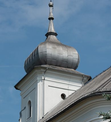 Zdjęcie nr 16: Murowany kościół otrzymał układ jednonawowej świątyni z węższym prezbiterium zwróconym ku północy i wieżą dostawioną do nawy od południa. Prezbiterium jest jednoprzęsłowe zakończone spłaszczoną apsydą. Na jego przedłużeniu usytuowano czworoboczną zakrystię. Prostokątna nawa jest trójprzęsłowa o zaokrąglonych narożnikach. Od frontu wzniesiono czworoboczną wieżę o ściętych narożnikach, flankowaną piętrowymi lokalnościami. Wysunięto ją lekko ku przodowi, gdzie przechodzi wklęsłymi płaszczyznami w boczne części fasady. Jej górne piętro nakryte cebulastym hełmem zostało opięte po bokach wolutami, obok których ustawiono kamienne klasycystyczne wazy. Elewacje zewnętrzne artykułowano podziałami ramowymi, zamykając wysokości ścian gzymsem gurtowy. Na końcu nawy na siodłowym dachu pokrytym blachą umieszczono czworoboczną wieżyczkę na sygnaturkę zwieńczoną cebulastym hełmem z krzyżem. Podobnym dachem nakryto prezbiterium. Wnętrze kościoła zostało rozczłonkowane lizenami z wklęsłymi półlizenami po bokach, ponad którymi rozciągnięto odcinki belkowania. Całość nakryto sklepieniem żaglastym na zdwojonych gurtach. Od południa w nawie urządzono chór muzyczny wsparty na dwóch kolumnach z parapetem wklęsłowypukłym. W prezbiterium usytuowano ołtarz główny, a w nawie dwa ołtarze boczne. Tu także na ścianie zachodniej zawieszono ambonę.  