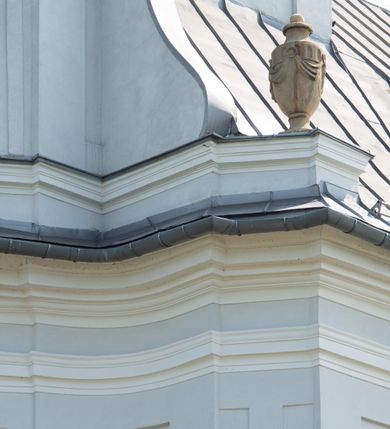 Zdjęcie nr 18: Murowany kościół otrzymał układ jednonawowej świątyni z węższym prezbiterium zwróconym ku północy i wieżą dostawioną do nawy od południa. Prezbiterium jest jednoprzęsłowe zakończone spłaszczoną apsydą. Na jego przedłużeniu usytuowano czworoboczną zakrystię. Prostokątna nawa jest trójprzęsłowa o zaokrąglonych narożnikach. Od frontu wzniesiono czworoboczną wieżę o ściętych narożnikach, flankowaną piętrowymi lokalnościami. Wysunięto ją lekko ku przodowi, gdzie przechodzi wklęsłymi płaszczyznami w boczne części fasady. Jej górne piętro nakryte cebulastym hełmem zostało opięte po bokach wolutami, obok których ustawiono kamienne klasycystyczne wazy. Elewacje zewnętrzne artykułowano podziałami ramowymi, zamykając wysokości ścian gzymsem gurtowy. Na końcu nawy na siodłowym dachu pokrytym blachą umieszczono czworoboczną wieżyczkę na sygnaturkę zwieńczoną cebulastym hełmem z krzyżem. Podobnym dachem nakryto prezbiterium. Wnętrze kościoła zostało rozczłonkowane lizenami z wklęsłymi półlizenami po bokach, ponad którymi rozciągnięto odcinki belkowania. Całość nakryto sklepieniem żaglastym na zdwojonych gurtach. Od południa w nawie urządzono chór muzyczny wsparty na dwóch kolumnach z parapetem wklęsłowypukłym. W prezbiterium usytuowano ołtarz główny, a w nawie dwa ołtarze boczne. Tu także na ścianie zachodniej zawieszono ambonę.  