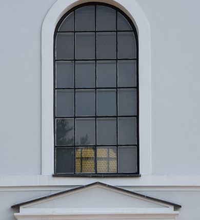 Zdjęcie nr 22: Murowany kościół otrzymał układ jednonawowej świątyni z węższym prezbiterium zwróconym ku północy i wieżą dostawioną do nawy od południa. Prezbiterium jest jednoprzęsłowe zakończone spłaszczoną apsydą. Na jego przedłużeniu usytuowano czworoboczną zakrystię. Prostokątna nawa jest trójprzęsłowa o zaokrąglonych narożnikach. Od frontu wzniesiono czworoboczną wieżę o ściętych narożnikach, flankowaną piętrowymi lokalnościami. Wysunięto ją lekko ku przodowi, gdzie przechodzi wklęsłymi płaszczyznami w boczne części fasady. Jej górne piętro nakryte cebulastym hełmem zostało opięte po bokach wolutami, obok których ustawiono kamienne klasycystyczne wazy. Elewacje zewnętrzne artykułowano podziałami ramowymi, zamykając wysokości ścian gzymsem gurtowy. Na końcu nawy na siodłowym dachu pokrytym blachą umieszczono czworoboczną wieżyczkę na sygnaturkę zwieńczoną cebulastym hełmem z krzyżem. Podobnym dachem nakryto prezbiterium. Wnętrze kościoła zostało rozczłonkowane lizenami z wklęsłymi półlizenami po bokach, ponad którymi rozciągnięto odcinki belkowania. Całość nakryto sklepieniem żaglastym na zdwojonych gurtach. Od południa w nawie urządzono chór muzyczny wsparty na dwóch kolumnach z parapetem wklęsłowypukłym. W prezbiterium usytuowano ołtarz główny, a w nawie dwa ołtarze boczne. Tu także na ścianie zachodniej zawieszono ambonę.  