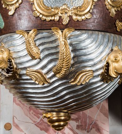 Zdjęcie nr 4: Rokokowa ambona przyścienna uzyskała kształt ożaglowanego okrętu. Składa się z kosza w formie beczkowej łodzi oraz zaplecka w kształcie żagla przechodzącego w baldachim. Kosz został podzielony na dwie strefy. W dolnej przedstawiono stylizowane, srebrzone fale morskie z igrającymi w nich morskimi, złoconymi stworami. Jeden z nich połyka postać Jonasza. Natomiast górną strefę udekorowano złoconymi, rokokowymi kartuszami, skrzyżowanymi dwoma wiosłami okrytymi fragmentem sieci rybackiej na brązowym tle. Z prawej strony do kosza przymocowano złoconą wolutę zdobioną motywem rocalliowym przechodzącym w srebrzony sztandar przymocowany do złotej laski krzyżowej. W zaplecek ambony w kształcie srebrzonego, rozpostartego żagla wstawiono nowy obraz w kształcie stojącego prostokąta, ukazujący błogosławiącego Chrystusa. Zbawiciel został przedstawiony frontalnie w dwóch trzecich postaci z głową i spojrzeniem skierowanym w górę. Prawą ręką błogosławi, lewą zaś przyciska do piersi. Jezus ma pociągłą twarz o wydatnym nosie i ustach, otoczoną brodą i długimi włosami spływającymi na ramiona. Ubrany jest w białą tunikę oraz w przerzucony przez ramię czerwony płaszcz. Jego głowę okala świetlisty nimb na ciemnym tle. Powyżej rozpięty jest baldachim utworzony z masztu podtrzymywanego przez liny i zwisających żagli zakończonych motywem lambrekinowym. Na baldachimie stoi postać uskrzydlonego anioła w luźnej, niebieskiej tunice. Ponad nim na złoconym maszcie umieszczone dwie korony, jedna nad drugą. Na jego szczycie znajduje się gloria z Duchem Świętym w postaci gołębicy na tle srebrzystych obłoków i złotych promieni. Od wschodu do ambony przylegają schody z pełną balustradą artykułowaną romboidalnym płycinami o złoconych krawędziach z polem wypełnionym złoconym motywem rocalliowym. 