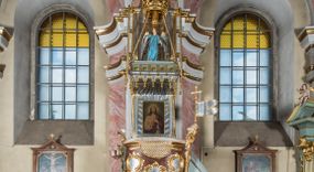 Zdjęcie nr 1: Rokokowa ambona przyścienna uzyskała kształt ożaglowanego okrętu. Składa się z kosza w formie beczkowej łodzi oraz zaplecka w kształcie żagla przechodzącego w baldachim. Kosz został podzielony na dwie strefy. W dolnej przedstawiono stylizowane, srebrzone fale morskie z igrającymi w nich morskimi, złoconymi stworami. Jeden z nich połyka postać Jonasza. Natomiast górną strefę udekorowano złoconymi, rokokowymi kartuszami, skrzyżowanymi dwoma wiosłami okrytymi fragmentem sieci rybackiej na brązowym tle. Z prawej strony do kosza przymocowano złoconą wolutę zdobioną motywem rocalliowym przechodzącym w srebrzony sztandar przymocowany do złotej laski krzyżowej. W zaplecek ambony w kształcie srebrzonego, rozpostartego żagla wstawiono nowy obraz w kształcie stojącego prostokąta, ukazujący błogosławiącego Chrystusa. Zbawiciel został przedstawiony frontalnie w dwóch trzecich postaci z głową i spojrzeniem skierowanym w górę. Prawą ręką błogosławi, lewą zaś przyciska do piersi. Jezus ma pociągłą twarz o wydatnym nosie i ustach, otoczoną brodą i długimi włosami spływającymi na ramiona. Ubrany jest w białą tunikę oraz w przerzucony przez ramię czerwony płaszcz. Jego głowę okala świetlisty nimb na ciemnym tle. Powyżej rozpięty jest baldachim utworzony z masztu podtrzymywanego przez liny i zwisających żagli zakończonych motywem lambrekinowym. Na baldachimie stoi postać uskrzydlonego anioła w luźnej, niebieskiej tunice. Ponad nim na złoconym maszcie umieszczone dwie korony, jedna nad drugą. Na jego szczycie znajduje się gloria z Duchem Świętym w postaci gołębicy na tle srebrzystych obłoków i złotych promieni. Od wschodu do ambony przylegają schody z pełną balustradą artykułowaną romboidalnym płycinami o złoconych krawędziach z polem wypełnionym złoconym motywem rocalliowym. 