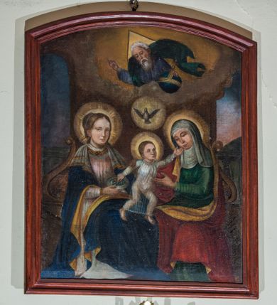 Zdjęcie nr 1: Obraz uzyskał kształt stojącego prostokąta zamkniętego od góry łukiem odcinkowym, ujęty w profilowaną, bejcowaną ramę. W centrum kompozycji wyobrażono siedzące na wspólnej ławie Matkę Boską i św. Annę, pomiędzy którymi znajduje się Dzieciątko Jezus. Ława została zaopatrzona w dwa wolutowe podłokietniki. Siedzącą Marię ujęto w trzech czwartych w prawo. Madonna prawą ręką trzyma srebrny talerz z winnym gronem. Ma pociągłą twarz z wydatnym nosem i ustami oraz spojrzeniem skierowanym w stronę widza. Brązowe włosy ma upięte w koka oplecionego sznurem pereł. Maria ubrana jest w bladoróżową suknię lamowaną pod szyją taśmą z naśladowaniem kameryzacji. Na szyi widoczny jest sznur pereł. Na ramionach narzucony ma ciemnoniebieski płaszcz podbity jasna ochrą, na którym znajduje się biała chusta dekorowana po bokach złotym obszyciem. Wokół głowy Matki Boskiej widoczny jest świetlisty nimb. Na jej kolanach stoi w rozkroku mały Jezus, który lewą rękę wyciąga w stronę św. Anny, a prawą bierze winne grono z talerza trzymanego przez matkę. Dzieciątko ujęte w trzech czwartych ma nieznacznie podniesioną głowę. Jego twarz jest owalna o jasnej karnacji. Głowę Jezusa okalają krótkie brązowe włosy odsłaniające fragment prawego ucha oraz świetlisty nimb. Zbawiciel ma ubraną na sobie przeźroczystą tunikę odsłaniającą bose stopy. Siedząca obok św. Anna ujęta została w trzech czwartych w lewo. Prawą ręką obejmuje Jezusa za ramię, lewą zaś ma wyciągniętą w jego stronę. Anna ma owalną twarz o jasnej karnacji z wydatnym nosem i wargami. Na głowie ma białą chustę oraz podwikę. Anna ubrana jest w zieloną suknię oraz narzucony na ramiona czerwony płaszcz podbity jasną ochrą. Także jej głowę okala świetlisty nimb. Pomiędzy głowami obu niewiast widnieje gołębica Ducha Świętego w świetlistym otoku. Powyżej z obłoków wyłania się w półpostaci Bóg Ojciec. Prawą ręką udziela błogosławieństwa, natomiast lewą podtrzymuje  niebieski glob ze złotym krzyżykiem. Jest to starszy mężczyzna o pociągłej twarzy okolonej siwą brodą i włosami. Jego twarz charakteryzuje się wydatnym nosem i ustami. W głębi widoczne są dwie półkoliste arkady z uproszczonymi sekwencjami pejzażowymi. 