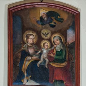 Zdjęcie nr 1: Obraz uzyskał kształt stojącego prostokąta zamkniętego od góry łukiem odcinkowym, ujęty w profilowaną, bejcowaną ramę. W centrum kompozycji wyobrażono siedzące na wspólnej ławie Matkę Boską i św. Annę, pomiędzy którymi znajduje się Dzieciątko Jezus. Ława została zaopatrzona w dwa wolutowe podłokietniki. Siedzącą Marię ujęto w trzech czwartych w prawo. Madonna prawą ręką trzyma srebrny talerz z winnym gronem. Ma pociągłą twarz z wydatnym nosem i ustami oraz spojrzeniem skierowanym w stronę widza. Brązowe włosy ma upięte w koka oplecionego sznurem pereł. Maria ubrana jest w bladoróżową suknię lamowaną pod szyją taśmą z naśladowaniem kameryzacji. Na szyi widoczny jest sznur pereł. Na ramionach narzucony ma ciemnoniebieski płaszcz podbity jasna ochrą, na którym znajduje się biała chusta dekorowana po bokach złotym obszyciem. Wokół głowy Matki Boskiej widoczny jest świetlisty nimb. Na jej kolanach stoi w rozkroku mały Jezus, który lewą rękę wyciąga w stronę św. Anny, a prawą bierze winne grono z talerza trzymanego przez matkę. Dzieciątko ujęte w trzech czwartych ma nieznacznie podniesioną głowę. Jego twarz jest owalna o jasnej karnacji. Głowę Jezusa okalają krótkie brązowe włosy odsłaniające fragment prawego ucha oraz świetlisty nimb. Zbawiciel ma ubraną na sobie przeźroczystą tunikę odsłaniającą bose stopy. Siedząca obok św. Anna ujęta została w trzech czwartych w lewo. Prawą ręką obejmuje Jezusa za ramię, lewą zaś ma wyciągniętą w jego stronę. Anna ma owalną twarz o jasnej karnacji z wydatnym nosem i wargami. Na głowie ma białą chustę oraz podwikę. Anna ubrana jest w zieloną suknię oraz narzucony na ramiona czerwony płaszcz podbity jasną ochrą. Także jej głowę okala świetlisty nimb. Pomiędzy głowami obu niewiast widnieje gołębica Ducha Świętego w świetlistym otoku. Powyżej z obłoków wyłania się w półpostaci Bóg Ojciec. Prawą ręką udziela błogosławieństwa, natomiast lewą podtrzymuje  niebieski glob ze złotym krzyżykiem. Jest to starszy mężczyzna o pociągłej twarzy okolonej siwą brodą i włosami. Jego twarz charakteryzuje się wydatnym nosem i ustami. W głębi widoczne są dwie półkoliste arkady z uproszczonymi sekwencjami pejzażowymi. 