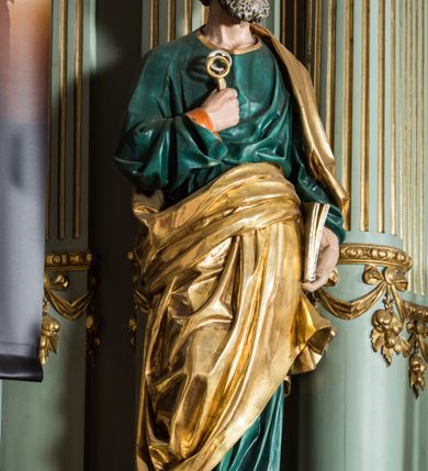 Zdjęcie nr 16: Ołtarz główny uzyskał formę przyściennej, dwukondygnacyjnej, neoklasycystycznej nastawy wzniesionej na rzucie elipsy z bocznymi bramkami. Stipes ołtarzowy uzyskał kształt leżącego prostopadłościanu podtrzymującego drewnianą mensę z portatylem. Jego lico dekorowane jest trzema równoległymi płycinami utworzonymi ze złoconych, profilowanych listew. Na mensie ustawiono prostopadłościenne tabernakulum w formie skrzynki flankowane parą pilastrów podtrzymujących nastawę tronu eucharystycznego. Ujmują go po bokach pary złoconych kolumn z korynckimi kapitelami podtrzymujące belkowanie wygięte na osi półkoliście. Na zwieńczeniu tabernakulum ustawiono leżącego na zamkniętej księdze z siedmioma pieczęciami srebrnego baranka apokaliptycznego na tle srebrzonych promieni. Pomiędzy kolumnami w polu zainstalowano obrotowy bęben z dwiema półkolistymi niszami. Retabulum zostało wsparte na wysokim cokole. Dolną kondygnację artykułują zwielokrotnione pilastry o kanelowanych trzonach i złoconych, kompozytowych głowicach oraz dwie wysunięte do przodu kanelowane kolumny o kapitelach kompozytowych. Podpory podtrzymują szeroki architraw wklęsło-wypukły dekorowany motywami roślinnymi oraz perełkami i ząbkami, wyłamany na przedłużeniu kolumn. W miejscu wyłamań usytuowano siedzących dwóch uskrzydlonych aniołów. Po bokach kolumn na konsolach ustawiono figury św. Piotra i św. Pawła. Boki ołtarza zamykają ażurowe wici roślinne pełniące rolę zredukowanych uszaków. W polu środkowym retabulum umieszczono prostokątne obramienie utworzone z dekoracyjnej ramy zdobionej wicią roślinną oraz podwieszonego u jej góry paludamentum z koroną podtrzymywaną przez dwa aniołki. W środku zainstalowano obraz Matki Boskiej Śnieżnej, a na zasuwie przedstawienie Chrztu Chrystusa w Jordanie. Zwieńczenie nastawy uzyskało kształt leżącego prostokąta flankowanego po bokach parą kanelowanych pilastrów o korynckich głowicach, na tle których ustawiono dwie kolumny podtrzymujących przerwane belkowanie z przerwanym przyczółkiem. Na osi zwieńczenia na postumencie ustawiono rzeźbę św. Michała Archanioła, a na przyczółkach rzeźby dwóch siedzących aniołów. W polu między pilastrami i kolumnami znalazło się płaskorzeźbione przedstawienie Trójcy Przenajświętszej. Dwie flankujące retabulum bramki ozdobiono dwoma aniołkami siedzącymi na ich zwieńczeniu na postumencie. Struktura całości pomalowane jest na zielono, ornamenty i profile wyzłocono, a rzeźby otrzymały naturalistyczną polichromię.