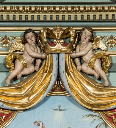 Zdjęcie nr 18: Ołtarz główny uzyskał formę przyściennej, dwukondygnacyjnej, neoklasycystycznej nastawy wzniesionej na rzucie elipsy z bocznymi bramkami. Stipes ołtarzowy uzyskał kształt leżącego prostopadłościanu podtrzymującego drewnianą mensę z portatylem. Jego lico dekorowane jest trzema równoległymi płycinami utworzonymi ze złoconych, profilowanych listew. Na mensie ustawiono prostopadłościenne tabernakulum w formie skrzynki flankowane parą pilastrów podtrzymujących nastawę tronu eucharystycznego. Ujmują go po bokach pary złoconych kolumn z korynckimi kapitelami podtrzymujące belkowanie wygięte na osi półkoliście. Na zwieńczeniu tabernakulum ustawiono leżącego na zamkniętej księdze z siedmioma pieczęciami srebrnego baranka apokaliptycznego na tle srebrzonych promieni. Pomiędzy kolumnami w polu zainstalowano obrotowy bęben z dwiema półkolistymi niszami. Retabulum zostało wsparte na wysokim cokole. Dolną kondygnację artykułują zwielokrotnione pilastry o kanelowanych trzonach i złoconych, kompozytowych głowicach oraz dwie wysunięte do przodu kanelowane kolumny o kapitelach kompozytowych. Podpory podtrzymują szeroki architraw wklęsło-wypukły dekorowany motywami roślinnymi oraz perełkami i ząbkami, wyłamany na przedłużeniu kolumn. W miejscu wyłamań usytuowano siedzących dwóch uskrzydlonych aniołów. Po bokach kolumn na konsolach ustawiono figury św. Piotra i św. Pawła. Boki ołtarza zamykają ażurowe wici roślinne pełniące rolę zredukowanych uszaków. W polu środkowym retabulum umieszczono prostokątne obramienie utworzone z dekoracyjnej ramy zdobionej wicią roślinną oraz podwieszonego u jej góry paludamentum z koroną podtrzymywaną przez dwa aniołki. W środku zainstalowano obraz Matki Boskiej Śnieżnej, a na zasuwie przedstawienie Chrztu Chrystusa w Jordanie. Zwieńczenie nastawy uzyskało kształt leżącego prostokąta flankowanego po bokach parą kanelowanych pilastrów o korynckich głowicach, na tle których ustawiono dwie kolumny podtrzymujących przerwane belkowanie z przerwanym przyczółkiem. Na osi zwieńczenia na postumencie ustawiono rzeźbę św. Michała Archanioła, a na przyczółkach rzeźby dwóch siedzących aniołów. W polu między pilastrami i kolumnami znalazło się płaskorzeźbione przedstawienie Trójcy Przenajświętszej. Dwie flankujące retabulum bramki ozdobiono dwoma aniołkami siedzącymi na ich zwieńczeniu na postumencie. Struktura całości pomalowane jest na zielono, ornamenty i profile wyzłocono, a rzeźby otrzymały naturalistyczną polichromię.