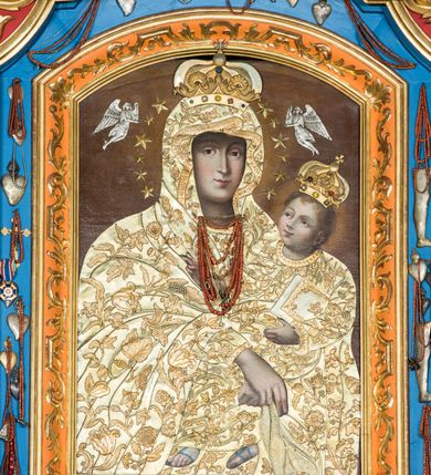 Zdjęcie nr 10: Ołtarz główny uzyskał formę przyściennej, dwukondygnacyjnej, neoklasycystycznej nastawy wzniesionej na rzucie elipsy z bocznymi bramkami. Stipes ołtarzowy uzyskał kształt leżącego prostopadłościanu podtrzymującego drewnianą mensę z portatylem. Jego lico dekorowane jest trzema równoległymi płycinami utworzonymi ze złoconych, profilowanych listew. Na mensie ustawiono prostopadłościenne tabernakulum w formie skrzynki flankowane parą pilastrów podtrzymujących nastawę tronu eucharystycznego. Ujmują go po bokach pary złoconych kolumn z korynckimi kapitelami podtrzymujące belkowanie wygięte na osi półkoliście. Na zwieńczeniu tabernakulum ustawiono leżącego na zamkniętej księdze z siedmioma pieczęciami srebrnego baranka apokaliptycznego na tle srebrzonych promieni. Pomiędzy kolumnami w polu zainstalowano obrotowy bęben z dwiema półkolistymi niszami. Retabulum zostało wsparte na wysokim cokole. Dolną kondygnację artykułują zwielokrotnione pilastry o kanelowanych trzonach i złoconych, kompozytowych głowicach oraz dwie wysunięte do przodu kanelowane kolumny o kapitelach kompozytowych. Podpory podtrzymują szeroki architraw wklęsło-wypukły dekorowany motywami roślinnymi oraz perełkami i ząbkami, wyłamany na przedłużeniu kolumn. W miejscu wyłamań usytuowano siedzących dwóch uskrzydlonych aniołów. Po bokach kolumn na konsolach ustawiono figury św. Piotra i św. Pawła. Boki ołtarza zamykają ażurowe wici roślinne pełniące rolę zredukowanych uszaków. W polu środkowym retabulum umieszczono prostokątne obramienie utworzone z dekoracyjnej ramy zdobionej wicią roślinną oraz podwieszonego u jej góry paludamentum z koroną podtrzymywaną przez dwa aniołki. W środku zainstalowano obraz Matki Boskiej Śnieżnej, a na zasuwie przedstawienie Chrztu Chrystusa w Jordanie. Zwieńczenie nastawy uzyskało kształt leżącego prostokąta flankowanego po bokach parą kanelowanych pilastrów o korynckich głowicach, na tle których ustawiono dwie kolumny podtrzymujących przerwane belkowanie z przerwanym przyczółkiem. Na osi zwieńczenia na postumencie ustawiono rzeźbę św. Michała Archanioła, a na przyczółkach rzeźby dwóch siedzących aniołów. W polu między pilastrami i kolumnami znalazło się płaskorzeźbione przedstawienie Trójcy Przenajświętszej. Dwie flankujące retabulum bramki ozdobiono dwoma aniołkami siedzącymi na ich zwieńczeniu na postumencie. Struktura całości pomalowane jest na zielono, ornamenty i profile wyzłocono, a rzeźby otrzymały naturalistyczną polichromię.