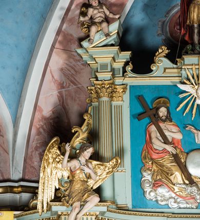 Zdjęcie nr 12: Ołtarz główny uzyskał formę przyściennej, dwukondygnacyjnej, neoklasycystycznej nastawy wzniesionej na rzucie elipsy z bocznymi bramkami. Stipes ołtarzowy uzyskał kształt leżącego prostopadłościanu podtrzymującego drewnianą mensę z portatylem. Jego lico dekorowane jest trzema równoległymi płycinami utworzonymi ze złoconych, profilowanych listew. Na mensie ustawiono prostopadłościenne tabernakulum w formie skrzynki flankowane parą pilastrów podtrzymujących nastawę tronu eucharystycznego. Ujmują go po bokach pary złoconych kolumn z korynckimi kapitelami podtrzymujące belkowanie wygięte na osi półkoliście. Na zwieńczeniu tabernakulum ustawiono leżącego na zamkniętej księdze z siedmioma pieczęciami srebrnego baranka apokaliptycznego na tle srebrzonych promieni. Pomiędzy kolumnami w polu zainstalowano obrotowy bęben z dwiema półkolistymi niszami. Retabulum zostało wsparte na wysokim cokole. Dolną kondygnację artykułują zwielokrotnione pilastry o kanelowanych trzonach i złoconych, kompozytowych głowicach oraz dwie wysunięte do przodu kanelowane kolumny o kapitelach kompozytowych. Podpory podtrzymują szeroki architraw wklęsło-wypukły dekorowany motywami roślinnymi oraz perełkami i ząbkami, wyłamany na przedłużeniu kolumn. W miejscu wyłamań usytuowano siedzących dwóch uskrzydlonych aniołów. Po bokach kolumn na konsolach ustawiono figury św. Piotra i św. Pawła. Boki ołtarza zamykają ażurowe wici roślinne pełniące rolę zredukowanych uszaków. W polu środkowym retabulum umieszczono prostokątne obramienie utworzone z dekoracyjnej ramy zdobionej wicią roślinną oraz podwieszonego u jej góry paludamentum z koroną podtrzymywaną przez dwa aniołki. W środku zainstalowano obraz Matki Boskiej Śnieżnej, a na zasuwie przedstawienie Chrztu Chrystusa w Jordanie. Zwieńczenie nastawy uzyskało kształt leżącego prostokąta flankowanego po bokach parą kanelowanych pilastrów o korynckich głowicach, na tle których ustawiono dwie kolumny podtrzymujących przerwane belkowanie z przerwanym przyczółkiem. Na osi zwieńczenia na postumencie ustawiono rzeźbę św. Michała Archanioła, a na przyczółkach rzeźby dwóch siedzących aniołów. W polu między pilastrami i kolumnami znalazło się płaskorzeźbione przedstawienie Trójcy Przenajświętszej. Dwie flankujące retabulum bramki ozdobiono dwoma aniołkami siedzącymi na ich zwieńczeniu na postumencie. Struktura całości pomalowane jest na zielono, ornamenty i profile wyzłocono, a rzeźby otrzymały naturalistyczną polichromię.