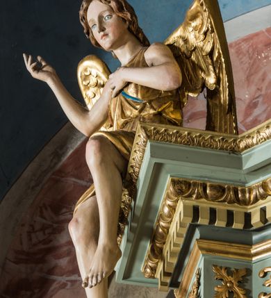 Zdjęcie nr 27: Ołtarz główny uzyskał formę przyściennej, dwukondygnacyjnej, neoklasycystycznej nastawy wzniesionej na rzucie elipsy z bocznymi bramkami. Stipes ołtarzowy uzyskał kształt leżącego prostopadłościanu podtrzymującego drewnianą mensę z portatylem. Jego lico dekorowane jest trzema równoległymi płycinami utworzonymi ze złoconych, profilowanych listew. Na mensie ustawiono prostopadłościenne tabernakulum w formie skrzynki flankowane parą pilastrów podtrzymujących nastawę tronu eucharystycznego. Ujmują go po bokach pary złoconych kolumn z korynckimi kapitelami podtrzymujące belkowanie wygięte na osi półkoliście. Na zwieńczeniu tabernakulum ustawiono leżącego na zamkniętej księdze z siedmioma pieczęciami srebrnego baranka apokaliptycznego na tle srebrzonych promieni. Pomiędzy kolumnami w polu zainstalowano obrotowy bęben z dwiema półkolistymi niszami. Retabulum zostało wsparte na wysokim cokole. Dolną kondygnację artykułują zwielokrotnione pilastry o kanelowanych trzonach i złoconych, kompozytowych głowicach oraz dwie wysunięte do przodu kanelowane kolumny o kapitelach kompozytowych. Podpory podtrzymują szeroki architraw wklęsło-wypukły dekorowany motywami roślinnymi oraz perełkami i ząbkami, wyłamany na przedłużeniu kolumn. W miejscu wyłamań usytuowano siedzących dwóch uskrzydlonych aniołów. Po bokach kolumn na konsolach ustawiono figury św. Piotra i św. Pawła. Boki ołtarza zamykają ażurowe wici roślinne pełniące rolę zredukowanych uszaków. W polu środkowym retabulum umieszczono prostokątne obramienie utworzone z dekoracyjnej ramy zdobionej wicią roślinną oraz podwieszonego u jej góry paludamentum z koroną podtrzymywaną przez dwa aniołki. W środku zainstalowano obraz Matki Boskiej Śnieżnej, a na zasuwie przedstawienie Chrztu Chrystusa w Jordanie. Zwieńczenie nastawy uzyskało kształt leżącego prostokąta flankowanego po bokach parą kanelowanych pilastrów o korynckich głowicach, na tle których ustawiono dwie kolumny podtrzymujących przerwane belkowanie z przerwanym przyczółkiem. Na osi zwieńczenia na postumencie ustawiono rzeźbę św. Michała Archanioła, a na przyczółkach rzeźby dwóch siedzących aniołów. W polu między pilastrami i kolumnami znalazło się płaskorzeźbione przedstawienie Trójcy Przenajświętszej. Dwie flankujące retabulum bramki ozdobiono dwoma aniołkami siedzącymi na ich zwieńczeniu na postumencie. Struktura całości pomalowane jest na zielono, ornamenty i profile wyzłocono, a rzeźby otrzymały naturalistyczną polichromię.