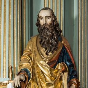 Zdjęcie nr 1: Pełnoplastyczna rzeźba św. Pawła ukazuje stojącego apostoła frontalnie w nieznacznym kontrapoście. Święty prawą rękę opiera na jelcu stojącego miecza, a w lewej opuszczonej wzdłuż tułowia trzyma zamkniętą księgę. Paweł ma pociągłą twarz o łysiejącym czole i ostrych rysach dojrzałego mężczyzny okoloną długą, mocno pofalowaną brodą i kędzierzawymi włosami. Charakteryzują ją wydatny nos i usta oraz spojrzenie szeroko otwartych oczu skierowane na widza. Apostoł ubrany jest w niebieską tunikę podbitą pomarańczem oraz w złoty płaszcz narzucony na ramiona i spięty na lewym barku z prawą połą owinięta wokół postaci. Płaszcz ma czerwone podbicie. Spod tuniki widać końcówki bosych stóp. 