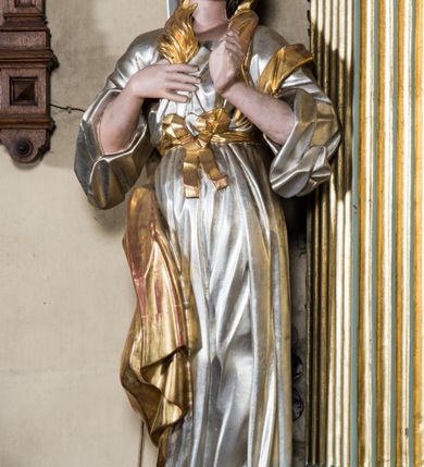 Zdjęcie nr 6: Wczesnoklasycystyczny, przyścienny ołtarz boczny, uzyskał kształt płaskiej nastawy jednokondygnacyjnej ze zwieńczeniem. Sarkofagowy stipes podtrzymuj drewnianą mensę przylegającą do wysokiego cokołu, na którym wzniesiono retabulum ujęte w boczne kanelowane pilastry o kompozytowych głowicach, podtrzymujących wyłamane po zewnętrznych belkowanie, dodatkowo wsparte w narożach na dwóch wolutowych konsolach dekorowanych motywem stylizowanej muszli. Na belkowaniu widoczny jest przerwany przyczółek, na którym usytuowano dwa siedzące, uskrzydlone aniołki. W polu między pilastrami usytuowano ornamentalną, czworoboczną ramę stanowiącą obramienie dla obrazu Matki Boskiej Różańcowej oraz umieszczonego na zasuwie obrazu Świętej Rodziny. Poniżej ramy zamontowano obraz Matki Boskiej Nieustającej Pomocy ujęty dwiema gablotami z wotami. Na tle pilastrów ustawiono dwie rzeźby niezidentyfikowanych świętych niewiast. Całoś dolnej kondygnacji flankują girlandy roślinno-kwiatowe pełniące rolę zredukowanych uszaków. Zwieńczenie nastawy uzyskało kształt leżącego prostokąta o wklęsłych bokach, zwieńczonego profilowanym gzymsem ujętym w nadwieszony łuk odcinkowy. Powyżej w promienistej glorii na tle obłoków wyobrażono trójkąt Bożej Opatrzności flankowany dwoma stojącymi aniołami. W polu zwieńczenia znalazła się prostokątna, płaskorzeźbiona płycina z monogramem maryjnym na tle słońca. Ponad nią widoczna jest para płaskorzeźbionych, uskrzydlonych główek anielskich. Struktura całości pomalowane jest na zielono, ornamenty i profile wyzłocono, a rzeźby otrzymały naturalistyczną polichromię.