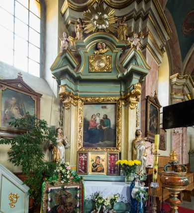 Zdjęcie nr 1: Wczesnoklasycystyczny, przyścienny ołtarz boczny, uzyskał kształt płaskiej nastawy jednokondygnacyjnej ze zwieńczeniem. Sarkofagowy stipes podtrzymuj drewnianą mensę przylegającą do wysokiego cokołu, na którym wzniesiono retabulum ujęte w boczne kanelowane pilastry o kompozytowych głowicach, podtrzymujących wyłamane po zewnętrznych belkowanie, dodatkowo wsparte w narożach na dwóch wolutowych konsolach dekorowanych motywem stylizowanej muszli. Na belkowaniu widoczny jest przerwany przyczółek, na którym usytuowano dwa siedzące, uskrzydlone aniołki. W polu między pilastrami usytuowano ornamentalną, czworoboczną ramę stanowiącą obramienie dla obrazu Matki Boskiej Różańcowej oraz umieszczonego na zasuwie obrazu Świętej Rodziny. Poniżej ramy zamontowano obraz Matki Boskiej Nieustającej Pomocy ujęty dwiema gablotami z wotami. Na tle pilastrów ustawiono dwie rzeźby niezidentyfikowanych świętych niewiast. Całoś dolnej kondygnacji flankują girlandy roślinno-kwiatowe pełniące rolę zredukowanych uszaków. Zwieńczenie nastawy uzyskało kształt leżącego prostokąta o wklęsłych bokach, zwieńczonego profilowanym gzymsem ujętym w nadwieszony łuk odcinkowy. Powyżej w promienistej glorii na tle obłoków wyobrażono trójkąt Bożej Opatrzności flankowany dwoma stojącymi aniołami. W polu zwieńczenia znalazła się prostokątna, płaskorzeźbiona płycina z monogramem maryjnym na tle słońca. Ponad nią widoczna jest para płaskorzeźbionych, uskrzydlonych główek anielskich. Struktura całości pomalowane jest na zielono, ornamenty i profile wyzłocono, a rzeźby otrzymały naturalistyczną polichromię.