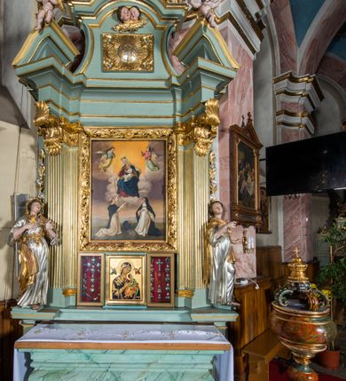Zdjęcie nr 7: Wczesnoklasycystyczny, przyścienny ołtarz boczny, uzyskał kształt płaskiej nastawy jednokondygnacyjnej ze zwieńczeniem. Sarkofagowy stipes podtrzymuj drewnianą mensę przylegającą do wysokiego cokołu, na którym wzniesiono retabulum ujęte w boczne kanelowane pilastry o kompozytowych głowicach, podtrzymujących wyłamane po zewnętrznych belkowanie, dodatkowo wsparte w narożach na dwóch wolutowych konsolach dekorowanych motywem stylizowanej muszli. Na belkowaniu widoczny jest przerwany przyczółek, na którym usytuowano dwa siedzące, uskrzydlone aniołki. W polu między pilastrami usytuowano ornamentalną, czworoboczną ramę stanowiącą obramienie dla obrazu Matki Boskiej Różańcowej oraz umieszczonego na zasuwie obrazu Świętej Rodziny. Poniżej ramy zamontowano obraz Matki Boskiej Nieustającej Pomocy ujęty dwiema gablotami z wotami. Na tle pilastrów ustawiono dwie rzeźby niezidentyfikowanych świętych niewiast. Całoś dolnej kondygnacji flankują girlandy roślinno-kwiatowe pełniące rolę zredukowanych uszaków. Zwieńczenie nastawy uzyskało kształt leżącego prostokąta o wklęsłych bokach, zwieńczonego profilowanym gzymsem ujętym w nadwieszony łuk odcinkowy. Powyżej w promienistej glorii na tle obłoków wyobrażono trójkąt Bożej Opatrzności flankowany dwoma stojącymi aniołami. W polu zwieńczenia znalazła się prostokątna, płaskorzeźbiona płycina z monogramem maryjnym na tle słońca. Ponad nią widoczna jest para płaskorzeźbionych, uskrzydlonych główek anielskich. Struktura całości pomalowane jest na zielono, ornamenty i profile wyzłocono, a rzeźby otrzymały naturalistyczną polichromię.