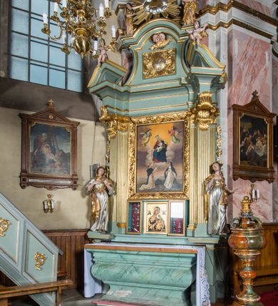 Zdjęcie nr 8: Wczesnoklasycystyczny, przyścienny ołtarz boczny, uzyskał kształt płaskiej nastawy jednokondygnacyjnej ze zwieńczeniem. Sarkofagowy stipes podtrzymuj drewnianą mensę przylegającą do wysokiego cokołu, na którym wzniesiono retabulum ujęte w boczne kanelowane pilastry o kompozytowych głowicach, podtrzymujących wyłamane po zewnętrznych belkowanie, dodatkowo wsparte w narożach na dwóch wolutowych konsolach dekorowanych motywem stylizowanej muszli. Na belkowaniu widoczny jest przerwany przyczółek, na którym usytuowano dwa siedzące, uskrzydlone aniołki. W polu między pilastrami usytuowano ornamentalną, czworoboczną ramę stanowiącą obramienie dla obrazu Matki Boskiej Różańcowej oraz umieszczonego na zasuwie obrazu Świętej Rodziny. Poniżej ramy zamontowano obraz Matki Boskiej Nieustającej Pomocy ujęty dwiema gablotami z wotami. Na tle pilastrów ustawiono dwie rzeźby niezidentyfikowanych świętych niewiast. Całoś dolnej kondygnacji flankują girlandy roślinno-kwiatowe pełniące rolę zredukowanych uszaków. Zwieńczenie nastawy uzyskało kształt leżącego prostokąta o wklęsłych bokach, zwieńczonego profilowanym gzymsem ujętym w nadwieszony łuk odcinkowy. Powyżej w promienistej glorii na tle obłoków wyobrażono trójkąt Bożej Opatrzności flankowany dwoma stojącymi aniołami. W polu zwieńczenia znalazła się prostokątna, płaskorzeźbiona płycina z monogramem maryjnym na tle słońca. Ponad nią widoczna jest para płaskorzeźbionych, uskrzydlonych główek anielskich. Struktura całości pomalowane jest na zielono, ornamenty i profile wyzłocono, a rzeźby otrzymały naturalistyczną polichromię.