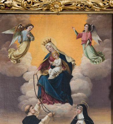 Zdjęcie nr 1: Obraz uzyskał kształt stojącego prostokąta. W centrum kompozycji przedstawiono Matkę Boską Różańcową w towarzystwie św. Dominika i św. Katarzyny Sieneńskiej. Siedząca na obłokach Madonna ukazana została frontalnie z głową pochyloną w lewo ujętą w trzech czwartych. Wyciągniętą prawą ręką podaje różaniec klęczącemu na ziemi św. Dominikowi, natomiast lewą przytrzymuje siedzącego na jej kolanach małego Jezusa. Maria ma pociągłą twarz o jasnej karnacji delikatny nos i usta oraz półprzymknięte oczy. Ubrana jest w szkarłatną suknię przepasaną w pasie oraz niebieski płaszcz podbity jasną ochrą, narzucony na ramiona i spięty pod szyją podłużną klamrą, którego lewa poła zakrywa jej kolana. Na głowie Maria ma jasną chustę, której rozwiane końce spływają na ramiona w całości zakrywając jej włosy. Na głowie otoczonej jasnym nimbem ma złotą koronę ze stylizowanymi floralnie sterczynami. Siedzące na kolanach matki Dzieciątko ujęte został w trzech czwartych w lewo. Jezus prawą ręką udziela błogosławieństwa Dominikowi, lewą zaś podtrzymuje na kolanach niebieski glob ze złotym krzyżykiem. Dzieciątko ma pociągłą twarz z drobnym nosem i ustami, otoczoną krótkimi jasnymi włosami odsłaniającymi fragment lewego ucha. Jego głowę okala świetlisty nimb. Klęczący z lewej strony św. Dominik został ukazany w trzech czwartych w prawo, z głową w profilu uniesioną w stronę Madonny. Obiema rękami odbiera różaniec od Marii zakończony złotym krzyżykiem. Jest to mężczyzna w średnim wieku o jasnej karnacji z siwiejącymi włosami z wyciętą tonsurą. Ma prosty nos i wydatne usta. Ubrany jest w biały habit i czarny płaszcz zakonny z kapturem. Wokół głowy widać nimb. Po drugiej stronie klęczy zwrócona w lewo św. Katarzyna ze Sieny. Prawą rękę przykłada do piersi, lewą zaś wyraźnie odsuwa od siebie w geście adoracji. Jej spojrzenie lekko uniesionej głowy jest skierowane w stronę Madonny. Katarzyna ma jasną karnację, drobny nos i usta. Święta ubrana jest w biały habit ze szkaplerzem oraz czarny welon, spod którego widać kornet i podwikę. Na głowie ma cierniową koronę. Jej głowę otacza nimb. W górnej części obrazu na tle obłoków ukazano dwóch adorujących Marię uskrzydlonych aniołów. Obaj ujęci zostali w pełnej postaci w trzech czwartych. Anioł z lewej pochyla głowę do przodu, trzymając w prawej ręce lilię, lewą zaś przykładając do piersi. Ubrany jest w długą jasną tunikę oraz bladoniebieską koszulę. Z kolei anioł z prawej unosi głowę ku górze, jednocześnie trzymając w lewej ręce złote berło. Na dole obrazu pomiędzy obu świętymi na tle łąki z widocznym w głębi górzystym krajobrazem leży otwarta księga oraz w tyle czarny pies z pochodnią w pysku, ukazany na tle globu.