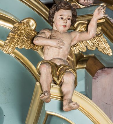 Zdjęcie nr 11: Przyścienny, wczesnoklasycystyczny ołtarz uzyskał formę architektonicznej, jednokondygnacyjnej nastawy ze zwieńczeniem. Sarkofagowy stipes ołtarzowy podtrzymuje drewnianą mensy, na której ustawiono prostopadłościenne tabernakulum w formie skrzynki. Złocone drzwiczki ozdobiono płaskorzeźbionym przedstawieniem kielicha ustawionego na obłokach z hostią otoczoną promieniami. Tabernakulum flankują dwie wypukło wklęsłe płyciny zawierające obraz ze scena pokłonu Trzech Króli oraz Zmartwychwstanie Chrystusa. Powyżej wzniesiono retabulum artykułowane po bokach kanelowanymi pilastrami z kompozytowymi głowicami, podtrzymującymi wyłamane po zewnętrznych belkowanie, dodatkowo wsparte na ustawionych w narożach konsolach. Konsole ozdobiono ornament z motywem  stylizowanej muszli. Na belkowaniu wsparto przerwany przyczółek, na bokach którego siedzą dwa uskrzydlone anioły. Zwieńczenie utworzono z lezącego prostokąta o wklęsłych bokach zwieńczonego profilowanym gzymsem ujętym w nadwieszony łuk odcinkowy. Na jego szczycie po bokach ustawiono dwa stojące uskrzydlone anioły. W polu zwieńczenia znalazł się płaskorzeźbiony chrystogram "IHS" w promienistej glorii. Powyżej umieszczono parę uskrzydlonych główek anielskich. Z kolei w polu kondygnacji między pilastrami usytuowano półokrągłą niszę z figurą Najświętszego Serca Pana Jezusa. Na tle pilastrów dostawione zostały posągi św. Barbary i św. Marii Magdaleny. Struktura została pomalowana w kolorze jasnego seledynu, ornamenty i profile wyzłocono, a rzeźby otrzymały naturalistyczną polichromię.