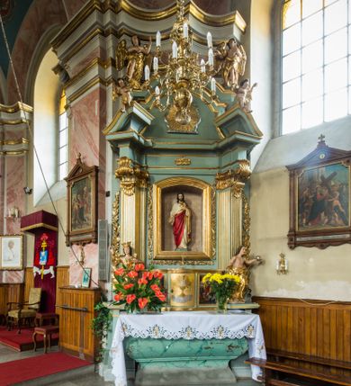 Zdjęcie nr 1: Przyścienny, wczesnoklasycystyczny ołtarz uzyskał formę architektonicznej, jednokondygnacyjnej nastawy ze zwieńczeniem. Sarkofagowy stipes ołtarzowy podtrzymuje drewnianą mensy, na której ustawiono prostopadłościenne tabernakulum w formie skrzynki. Złocone drzwiczki ozdobiono płaskorzeźbionym przedstawieniem kielicha ustawionego na obłokach z hostią otoczoną promieniami. Tabernakulum flankują dwie wypukło wklęsłe płyciny zawierające obraz ze scena pokłonu Trzech Króli oraz Zmartwychwstanie Chrystusa. Powyżej wzniesiono retabulum artykułowane po bokach kanelowanymi pilastrami z kompozytowymi głowicami, podtrzymującymi wyłamane po zewnętrznych belkowanie, dodatkowo wsparte na ustawionych w narożach konsolach. Konsole ozdobiono ornament z motywem  stylizowanej muszli. Na belkowaniu wsparto przerwany przyczółek, na bokach którego siedzą dwa uskrzydlone anioły. Zwieńczenie utworzono z lezącego prostokąta o wklęsłych bokach zwieńczonego profilowanym gzymsem ujętym w nadwieszony łuk odcinkowy. Na jego szczycie po bokach ustawiono dwa stojące uskrzydlone anioły. W polu zwieńczenia znalazł się płaskorzeźbiony chrystogram "IHS" w promienistej glorii. Powyżej umieszczono parę uskrzydlonych główek anielskich. Z kolei w polu kondygnacji między pilastrami usytuowano półokrągłą niszę z figurą Najświętszego Serca Pana Jezusa. Na tle pilastrów dostawione zostały posągi św. Barbary i św. Marii Magdaleny. Struktura została pomalowana w kolorze jasnego seledynu, ornamenty i profile wyzłocono, a rzeźby otrzymały naturalistyczną polichromię.