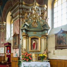 Zdjęcie nr 1: Przyścienny, wczesnoklasycystyczny ołtarz uzyskał formę architektonicznej, jednokondygnacyjnej nastawy ze zwieńczeniem. Sarkofagowy stipes ołtarzowy podtrzymuje drewnianą mensy, na której ustawiono prostopadłościenne tabernakulum w formie skrzynki. Złocone drzwiczki ozdobiono płaskorzeźbionym przedstawieniem kielicha ustawionego na obłokach z hostią otoczoną promieniami. Tabernakulum flankują dwie wypukło wklęsłe płyciny zawierające obraz ze scena pokłonu Trzech Króli oraz Zmartwychwstanie Chrystusa. Powyżej wzniesiono retabulum artykułowane po bokach kanelowanymi pilastrami z kompozytowymi głowicami, podtrzymującymi wyłamane po zewnętrznych belkowanie, dodatkowo wsparte na ustawionych w narożach konsolach. Konsole ozdobiono ornament z motywem  stylizowanej muszli. Na belkowaniu wsparto przerwany przyczółek, na bokach którego siedzą dwa uskrzydlone anioły. Zwieńczenie utworzono z lezącego prostokąta o wklęsłych bokach zwieńczonego profilowanym gzymsem ujętym w nadwieszony łuk odcinkowy. Na jego szczycie po bokach ustawiono dwa stojące uskrzydlone anioły. W polu zwieńczenia znalazł się płaskorzeźbiony chrystogram &quot;IHS&quot; w promienistej glorii. Powyżej umieszczono parę uskrzydlonych główek anielskich. Z kolei w polu kondygnacji między pilastrami usytuowano półokrągłą niszę z figurą Najświętszego Serca Pana Jezusa. Na tle pilastrów dostawione zostały posągi św. Barbary i św. Marii Magdaleny. Struktura została pomalowana w kolorze jasnego seledynu, ornamenty i profile wyzłocono, a rzeźby otrzymały naturalistyczną polichromię.