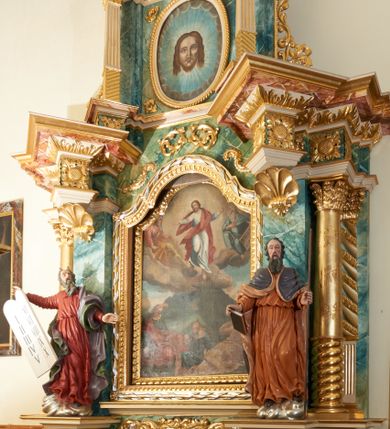 Zdjęcie nr 1: Obraz w kształcie stojącego prostokąta zamkniętego łukiem wklęsło-wypukłym z uskokami, ukazujący scenę Przemienienia na górze Tabor. U góry, pośrodku kompozycji pośród obłoków ukazany jest Chrystus  z szeroko rozłożonymi rękami, głową przechyloną w prawą stronę i prawą nogą ugiętą w kolanie. Ubrany jest w białą suknię i czerwony płaszcz. Po prawej stronie Zbawiciela siedzi prorok Eliasz, a po lewej Mojżesz, obaj przedstawieni na obłokach, zwróceni w stronę Chrystusa. Eliasz ubrany jest w czerwoną suknię i jasnobrązowy płaszcz, natomiast Mojżesz w niebieskie szaty, w dłoni trzyma tablice dekalogu. Poniżej na tle wzniesienia góry ukazani są w półleżących pozach św. Jan Ewangelista, św. Piotr oraz św. Jakub. Święty Piotr, przedstawiony pośrodku, ubrany jest w błękitną suknię i brązowy płaszcz zarzucony na plecy. Po prawej leży św. Jakub w beżowej sukni i płaszczu okrywającym nogi. Natomiast po lewej stronie kompozycji ukazany jest św. Jan Ewangelista w zielonej sukni i czerwonym płaszczu. Wszyscy o fizjonomiach dla nich charakterystycznych w ikonografii chrześcijańskiej: św. Jan – o fizjonomii młodzieńca, św. Jakuba – starca, św. Piotr – z łysiną i krótką brodą. W oddali widać górski krajobraz i miasto. Rama drewniana, pozłacana, ozdobiona geometrycznym kimationem. 