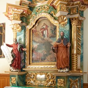 Zdjęcie nr 1: Obraz w kształcie stojącego prostokąta zamkniętego łukiem wklęsło-wypukłym z uskokami, ukazujący scenę Przemienienia na górze Tabor. U góry, pośrodku kompozycji pośród obłoków ukazany jest Chrystus  z szeroko rozłożonymi rękami, głową przechyloną w prawą stronę i prawą nogą ugiętą w kolanie. Ubrany jest w białą suknię i czerwony płaszcz. Po prawej stronie Zbawiciela siedzi prorok Eliasz, a po lewej Mojżesz, obaj przedstawieni na obłokach, zwróceni w stronę Chrystusa. Eliasz ubrany jest w czerwoną suknię i jasnobrązowy płaszcz, natomiast Mojżesz w niebieskie szaty, w dłoni trzyma tablice dekalogu. Poniżej na tle wzniesienia góry ukazani są w półleżących pozach św. Jan Ewangelista, św. Piotr oraz św. Jakub. Święty Piotr, przedstawiony pośrodku, ubrany jest w błękitną suknię i brązowy płaszcz zarzucony na plecy. Po prawej leży św. Jakub w beżowej sukni i płaszczu okrywającym nogi. Natomiast po lewej stronie kompozycji ukazany jest św. Jan Ewangelista w zielonej sukni i czerwonym płaszczu. Wszyscy o fizjonomiach dla nich charakterystycznych w ikonografii chrześcijańskiej: św. Jan – o fizjonomii młodzieńca, św. Jakuba – starca, św. Piotr – z łysiną i krótką brodą. W oddali widać górski krajobraz i miasto. Rama drewniana, pozłacana, ozdobiona geometrycznym kimationem. 