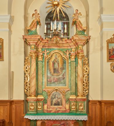 Zdjęcie nr 2: Nastawa ołtarzowa architektoniczna, jednoosiowa, jednokondygnacyjna. Ołtarz prostopadłościenny, drewniany, z drewnianą mensą na niskim cokole, flankowaną po bokach parą kanelowanych pilastrów o kapitelach jońskich. Antependium w formie płyciny marmoryzowanej na kolor różowy w kształcie leżącego prostokąta o owalnych narożach, ujęte w złoconą i wąską ramę. W polu płaskorzeźbione narzędzia Męki Pańskiej (krzyż, włócznia i korona cierniowa). 

Cokół nastawy zryzalitowany, wysoki, zdobiony płycinami z rozetami. Kondygnacja ujęta jest od wewnątrz parą pilastrów o kanelowanych trzonach, a od zewnątrz parą marmoryzowanych na zielono filarów i ustawioną przed nimi parą kolumn o kanelowanych i marmoryzowanych na różowo trzonach. Podpory ustawione są na bazach, mają kompozytowe kapitele i wspierają imposty oraz przerwane nad polem środkowym belkowanie, dekorowane profilowaniem i pasem kostkowania, a także przerwany, wolutowy przyczółek z parą aniołków. Nad środkiem belkowania nad dwóch niewielkich, spiętych spływach wolutowych ustawiona jest niewielkich rozmiarów rzeźbiona grupa przedstawiająca Boga Ojca po prawej i Jezusa Chrystusa po lewej stronie. Nad retabulum, nad wnęką okienną zawieszona jest gołębica Ducha Świętego w dużej promienistej glorii o promieniach, zebranych w wiązki nierównej długości. Retabulum po bokach ujęte jest uszami w formie ażurowej wici z ornamentu rocaille'owego.

W polu środkowym w szerokiej ramie w kształcie stojącego prostokąta, zamkniętego łukiem wklęsło-wypukłym z uskokami umieszczony jest obraz św. Mikołaja oraz św. Barbary na zasuwie. W zwieńczeniu ramy po bokach usadzona jest para aniołków. Poniżej obrazu fantazyjna, architektoniczna oprawa z umieszczonym w polu obrazem św. Teresy z Lisieux. Oprawa w formie niewielkiej, płaskiej aediculi, ustawionej na niskim cokole, flankowanej dwoma pilastrami, zamkniętej łukiem nadwieszonym, na szczycie którego niski cokolik na krucyfiks. Po bokach uszy o fantazyjnym wykroju, z wycięciem w górnej połowie, w dolnej zdobione kratką.

Struktura marmoryzowana jest w odcieniu niebieskim i jasnoróżowym; ornamentyka, profile, ramy i kanelury na pilastrach są złocone.