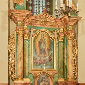 Zdjęcie nr 1: Nastawa ołtarzowa architektoniczna, jednoosiowa, jednokondygnacyjna. Ołtarz prostopadłościenny, drewniany, z drewnianą mensą na niskim cokole, flankowaną po bokach parą kanelowanych pilastrów o kapitelach jońskich. Antependium w formie płyciny marmoryzowanej na kolor różowy w kształcie leżącego prostokąta o owalnych narożach, ujęte w złoconą i wąską ramę. W polu płaskorzeźbione narzędzia Męki Pańskiej (krzyż, włócznia i korona cierniowa). 

Cokół nastawy zryzalitowany, wysoki, zdobiony płycinami z rozetami. Kondygnacja ujęta jest od wewnątrz parą pilastrów o kanelowanych trzonach, a od zewnątrz parą marmoryzowanych na zielono filarów i ustawioną przed nimi parą kolumn o kanelowanych i marmoryzowanych na różowo trzonach. Podpory ustawione są na bazach, mają kompozytowe kapitele i wspierają imposty oraz przerwane nad polem środkowym belkowanie, dekorowane profilowaniem i pasem kostkowania, a także przerwany, wolutowy przyczółek z parą aniołków. Nad środkiem belkowania nad dwóch niewielkich, spiętych spływach wolutowych ustawiona jest niewielkich rozmiarów rzeźbiona grupa przedstawiająca Boga Ojca po prawej i Jezusa Chrystusa po lewej stronie. Nad retabulum, nad wnęką okienną zawieszona jest gołębica Ducha Świętego w dużej promienistej glorii o promieniach, zebranych w wiązki nierównej długości. Retabulum po bokach ujęte jest uszami w formie ażurowej wici z ornamentu rocaille'owego.

W polu środkowym w szerokiej ramie w kształcie stojącego prostokąta, zamkniętego łukiem wklęsło-wypukłym z uskokami umieszczony jest obraz św. Mikołaja oraz św. Barbary na zasuwie. W zwieńczeniu ramy po bokach usadzona jest para aniołków. Poniżej obrazu fantazyjna, architektoniczna oprawa z umieszczonym w polu obrazem św. Teresy z Lisieux. Oprawa w formie niewielkiej, płaskiej aediculi, ustawionej na niskim cokole, flankowanej dwoma pilastrami, zamkniętej łukiem nadwieszonym, na szczycie którego niski cokolik na krucyfiks. Po bokach uszy o fantazyjnym wykroju, z wycięciem w górnej połowie, w dolnej zdobione kratką.

Struktura marmoryzowana jest w odcieniu niebieskim i jasnoróżowym; ornamentyka, profile, ramy i kanelury na pilastrach są złocone.