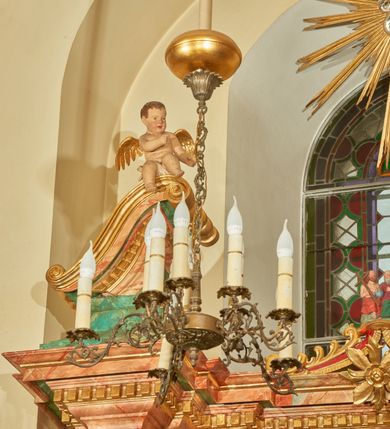 Zdjęcie nr 13: Nastawa ołtarzowa architektoniczna, jednoosiowa, jednokondygnacyjna. Ołtarz prostopadłościenny, drewniany, z drewnianą mensą na niskim cokole, flankowaną po bokach parą kanelowanych pilastrów o kapitelach jońskich. Antependium w formie płyciny marmoryzowanej na kolor różowy w kształcie leżącego prostokąta o owalnych narożach, ujęte w złoconą i wąską ramę. W polu płaskorzeźbione narzędzia Męki Pańskiej (krzyż, włócznia i korona cierniowa). 

Cokół nastawy zryzalitowany, wysoki, zdobiony płycinami z rozetami. Kondygnacja ujęta jest od wewnątrz parą pilastrów o kanelowanych trzonach, a od zewnątrz parą marmoryzowanych na zielono filarów i ustawioną przed nimi parą kolumn o kanelowanych i marmoryzowanych na różowo trzonach. Podpory ustawione są na bazach, mają kompozytowe kapitele i wspierają imposty oraz przerwane nad polem środkowym belkowanie, dekorowane profilowaniem i pasem kostkowania, a także przerwany, wolutowy przyczółek z parą aniołków. Nad środkiem belkowania nad dwóch niewielkich, spiętych spływach wolutowych ustawiona jest niewielkich rozmiarów rzeźbiona grupa przedstawiająca Boga Ojca po prawej i Jezusa Chrystusa po lewej stronie. Nad retabulum, nad wnęką okienną zawieszona jest gołębica Ducha Świętego w dużej promienistej glorii o promieniach, zebranych w wiązki nierównej długości. Retabulum po bokach ujęte jest uszami w formie ażurowej wici z ornamentu rocaille'owego.

W polu środkowym w szerokiej ramie w kształcie stojącego prostokąta, zamkniętego łukiem wklęsło-wypukłym z uskokami umieszczony jest obraz św. Mikołaja oraz św. Barbary na zasuwie. W zwieńczeniu ramy po bokach usadzona jest para aniołków. Poniżej obrazu fantazyjna, architektoniczna oprawa z umieszczonym w polu obrazem św. Teresy z Lisieux. Oprawa w formie niewielkiej, płaskiej aediculi, ustawionej na niskim cokole, flankowanej dwoma pilastrami, zamkniętej łukiem nadwieszonym, na szczycie którego niski cokolik na krucyfiks. Po bokach uszy o fantazyjnym wykroju, z wycięciem w górnej połowie, w dolnej zdobione kratką.

Struktura marmoryzowana jest w odcieniu niebieskim i jasnoróżowym; ornamentyka, profile, ramy i kanelury na pilastrach są złocone.