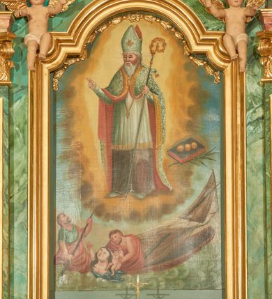 Zdjęcie nr 7: Nastawa ołtarzowa architektoniczna, jednoosiowa, jednokondygnacyjna. Ołtarz prostopadłościenny, drewniany, z drewnianą mensą na niskim cokole, flankowaną po bokach parą kanelowanych pilastrów o kapitelach jońskich. Antependium w formie płyciny marmoryzowanej na kolor różowy w kształcie leżącego prostokąta o owalnych narożach, ujęte w złoconą i wąską ramę. W polu płaskorzeźbione narzędzia Męki Pańskiej (krzyż, włócznia i korona cierniowa). 

Cokół nastawy zryzalitowany, wysoki, zdobiony płycinami z rozetami. Kondygnacja ujęta jest od wewnątrz parą pilastrów o kanelowanych trzonach, a od zewnątrz parą marmoryzowanych na zielono filarów i ustawioną przed nimi parą kolumn o kanelowanych i marmoryzowanych na różowo trzonach. Podpory ustawione są na bazach, mają kompozytowe kapitele i wspierają imposty oraz przerwane nad polem środkowym belkowanie, dekorowane profilowaniem i pasem kostkowania, a także przerwany, wolutowy przyczółek z parą aniołków. Nad środkiem belkowania nad dwóch niewielkich, spiętych spływach wolutowych ustawiona jest niewielkich rozmiarów rzeźbiona grupa przedstawiająca Boga Ojca po prawej i Jezusa Chrystusa po lewej stronie. Nad retabulum, nad wnęką okienną zawieszona jest gołębica Ducha Świętego w dużej promienistej glorii o promieniach, zebranych w wiązki nierównej długości. Retabulum po bokach ujęte jest uszami w formie ażurowej wici z ornamentu rocaille'owego.

W polu środkowym w szerokiej ramie w kształcie stojącego prostokąta, zamkniętego łukiem wklęsło-wypukłym z uskokami umieszczony jest obraz św. Mikołaja oraz św. Barbary na zasuwie. W zwieńczeniu ramy po bokach usadzona jest para aniołków. Poniżej obrazu fantazyjna, architektoniczna oprawa z umieszczonym w polu obrazem św. Teresy z Lisieux. Oprawa w formie niewielkiej, płaskiej aediculi, ustawionej na niskim cokole, flankowanej dwoma pilastrami, zamkniętej łukiem nadwieszonym, na szczycie którego niski cokolik na krucyfiks. Po bokach uszy o fantazyjnym wykroju, z wycięciem w górnej połowie, w dolnej zdobione kratką.

Struktura marmoryzowana jest w odcieniu niebieskim i jasnoróżowym; ornamentyka, profile, ramy i kanelury na pilastrach są złocone.