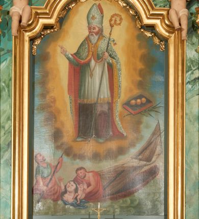 Zdjęcie nr 3: Obraz w kształcie stojącego prostokąta, zamkniętego łukiem wklęsło-wypukłym z uskokami z przedstawieniem św. Mikołaja ratującego rozbitków. Kompozycja dwustrefowa, wielopostaciowa. W górnej strefie, w centrum kompozycji św. Mikołaj ukazany na tle otoku utworzonego z światła i chmur, zwrócony trzy czwarte w prawo, który prawą ręką czyni gest błogosławieństwa, a w lewej trzyma pastorał. Święty ubrany jest w szaty biskupie: sięgającą do ziemi szarą albę, białą rokietę zakończoną złotą lamelką oraz ozdobny płaszcz z czerwoną podszewką i złotym galonem na obrzeżach; na głowie ma infułę. Twarz okolona jest siwą i długą brodą. Po prawej stronie obrazu znajduje się palma męczeństwa i zamknięta księga w ciemnej oprawie, a na niej ułożone rzędem trzy złote kule. W dolnej strefie, w morskiej fali, na zatopionej częściowo łódce z przewróconym, wysokim, białym żaglem widoczna jest grupka tonących ludzi. Po lewej mężczyzna siedzący na końcu łódki, zwrócony trzy czwarte w lewo, z wiosłem w rękach,  z głową skierowaną w stronę św. Mikołaja. Ubrany jest w niebieską suknię z podwiniętym rękawem oraz przerzucony przez lewe ramię czerwony płaszcz, okrywający prawie całą postać.  Twarz ukazana z prawego profilu, włosy i broda siwe, długi i wąski nos. Obok niego mężczyzna ukazany od pasa w górę, ratujący tonącą kobietę i dziecko. Ubrany jest w czerwoną szatę, zarzuconą na prawe ramię i otulającą prawie całą postać. Kobieta do piersi zanurzona w morskiej fali, zwrócona trzy czwarte w prawo, z rękoma wzniesionymi ku górze i głową skierowaną w stronę św. Mikołaja. Ubrana jest w niebieską szatę, odsłaniającą piersi. Twarz okrągła; małe usta; długi i wąski nos, niskie czoło. Włosy ciemne, długie, z przedziałkiem na środku. Na jej lewym ramieniu nagie niemowlę, zwrócone trzy czwarte w prawo, z rękoma wzniesionymi ku górze. Kolorystyka bogata, z przewagą barw błękitu i czerwieni. Rama drewniana, profilowana, złocona, od góry zamknięta łukiem wklęsło-wypukłym z uskokami i ozdobiona girlandą utworzoną z kampanul i kwiatów.