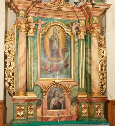 Zdjęcie nr 1: Obraz w kształcie stojącego prostokąta, zamkniętego łukiem wklęsło-wypukłym z uskokami z przedstawieniem św. Mikołaja ratującego rozbitków. Kompozycja dwustrefowa, wielopostaciowa. W górnej strefie, w centrum kompozycji św. Mikołaj ukazany na tle otoku utworzonego z światła i chmur, zwrócony trzy czwarte w prawo, który prawą ręką czyni gest błogosławieństwa, a w lewej trzyma pastorał. Święty ubrany jest w szaty biskupie: sięgającą do ziemi szarą albę, białą rokietę zakończoną złotą lamelką oraz ozdobny płaszcz z czerwoną podszewką i złotym galonem na obrzeżach; na głowie ma infułę. Twarz okolona jest siwą i długą brodą. Po prawej stronie obrazu znajduje się palma męczeństwa i zamknięta księga w ciemnej oprawie, a na niej ułożone rzędem trzy złote kule. W dolnej strefie, w morskiej fali, na zatopionej częściowo łódce z przewróconym, wysokim, białym żaglem widoczna jest grupka tonących ludzi. Po lewej mężczyzna siedzący na końcu łódki, zwrócony trzy czwarte w lewo, z wiosłem w rękach,  z głową skierowaną w stronę św. Mikołaja. Ubrany jest w niebieską suknię z podwiniętym rękawem oraz przerzucony przez lewe ramię czerwony płaszcz, okrywający prawie całą postać.  Twarz ukazana z prawego profilu, włosy i broda siwe, długi i wąski nos. Obok niego mężczyzna ukazany od pasa w górę, ratujący tonącą kobietę i dziecko. Ubrany jest w czerwoną szatę, zarzuconą na prawe ramię i otulającą prawie całą postać. Kobieta do piersi zanurzona w morskiej fali, zwrócona trzy czwarte w prawo, z rękoma wzniesionymi ku górze i głową skierowaną w stronę św. Mikołaja. Ubrana jest w niebieską szatę, odsłaniającą piersi. Twarz okrągła; małe usta; długi i wąski nos, niskie czoło. Włosy ciemne, długie, z przedziałkiem na środku. Na jej lewym ramieniu nagie niemowlę, zwrócone trzy czwarte w prawo, z rękoma wzniesionymi ku górze. Kolorystyka bogata, z przewagą barw błękitu i czerwieni. Rama drewniana, profilowana, złocona, od góry zamknięta łukiem wklęsło-wypukłym z uskokami i ozdobiona girlandą utworzoną z kampanul i kwiatów.