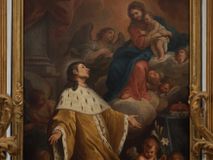 Zdjęcie nr 1: Obraz w kształcie stojącego prostokąta, w drewnianej, profilowanej, złoconej ramie ozdobionej motywami liści i kwiatów. Na obrazie przedstawiony klęczący św. Kazimierz, któremu ukazuje się siedząca na chmurach Matka Boska z Dzieciątkiem w otoczeniu aniołów. Święty ujęty w trzech czwartych, z rękami opuszczonymi w dół i rozłożonymi na boki, z głową niemalże z profilu zwróconą w górę, w kierunku Matki Boskiej. Jego twarz oddającą rysy młodego mężczyzny, wyróżniają wydatny nos, szeroko otwarte oczy i pełne, lekko rozwarte usta. Brązowe włosy, odsłaniające ucho, są lekko skręcone i sięgają ramion; wokół głowy zaznaczony rozświetlony nimb. Ubrany jest w długi,  jasnobrązowy płaszcz z gronostajowym, długim kołnierzem, gronostajowymi mankietami i brzegami. Maria przedstawiona jest w trzech czwartych, zwrócona w kierunku św. Kazimierza, o twarzy owalnej, miękko modelowanych rysach, z długim nosem i drobnymi, pełnymi ustami, z brązowymi włosami przykrytymi brązowym welonem. Jest ubrana w brązową koszulę z wąskimi rękawami, czerwoną suknię i niebieski płaszcz przerzucony na lewym ramieniu i prawej nodze. Trzymany przez nią Jezus stoi i został ukazany w trzech czwartych, z białą pieluchą wokół bioder. Zwraca się w kierunku świętego, unosząc prawą rączkę w geście błogosławieństwa, a lewą trzymając na ręce obejmującej go matki. Z chmur wyłaniają się uskrzydlone główki aniołków, o podobnych pełnych twarzach, różowych policzkach i drobnych ustach. W prawym, dolnym rogu kompozycji przed stolikiem nakrytym zielonym, długim obrusem z książęcą tiarą ukazane dwa nagie putta. Putto siedzące trzyma rozłożoną księgę z cytatem „Omni Die dic MARIAE mea laudes anima [E]ius festa [Eiu]s gesta [col]e devotissima”, na który wskazuje palcem drugi, stojący anioł, z zarzuconą zieloną szarfą, trzymający w ręku lilię. Za św. Kazimierzem, na tle kolumny przesłoniętej od góry czerwoną kotarą, stoi uskrzydlony anioł, z głową i lekko ugiętą prawą nogą zwróconą w lewo, a ciałem i złożonymi w geście modlitwy rękami w swoją prawą stronę. Anioł jest ubrany w białą suknię i turkusowy płaszcz. Drugi z aniołów wyłania się z chmur i zwraca w kierunku Marii, ukazany jest do pasa, w trzech czwartych, z rękami złożonymi na piersi, ubrany w białą suknię i zielony płaszcz. W tle kompozycji skłębione chmury rozświetlone słońcem.          