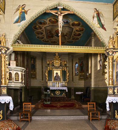 Zdjęcie nr 2: Kościół pomocniczny pw. Wniebowzięcia Najświętszej Marii Panny w Woli Radziszowskiej to niewielkich rozmiarów, orientowana, jednonawowa budowla drewniana, konstrukcji zrębowej, z wieżą w słup. Prezbiterium jest zamknięte wielobocznie, nieco wyższa i szersza nawa ma rzut prostokąta zbliżonego do kwadratu. Do prezbiterium od strony północnej przylega zakrystia, od wschodniej Ogrójec, przy nawie od południa umieszczona została niewielka, prostokątna kruchta. Od zachodu do budowli dostawiona jest czworoboczna wieża o pochyłych ścianach, z podwieszoną izbicą z czworobocznymi występami na przekątnikach; hełm ostrosłupowy z czterema wieżyczkami na występach. W przyziemiu wieży znajduje się kruchta, a dookoła wieży szalowane soboty. Wewnątrz świątyni stropy; w nawie z zaskrzynieniami. Otwór tęczowy ma kształt ostrołuku, belka jest profilowana, na niej umieszczony jest krucyfiks o charakterze późnogotyckim. Chór muzyczny w zachodniej części nawy jest drewniany, wsparty na dwóch kolumnach. Okna nawy i prezbiterium są głównie prostokątne zamknięte półkoliście; z witrażami (z wyjątkiem okna za ołtarzem głównym); ponadto budowlę doświetlają niewielkie okienka prostokątne. Do świątyni prowadzi dwoje drzwi ostrołukowych, trzecie od strony zachodniej przerobiono w 1933 roku. Dachy kościoła są kryte gontem, ponad nawą i kruchtą południową dwuspadowe, nad zakrystią jednospadowy, nad prezbiterium wielopołaciowy. Wieżyczka na sygnaturkę o formach barokowych z glorietą, cebulastym hełmem zwieńczonym kulą oraz krzyżem; kryta blachą. Świątynia usytuowana jest na niewielkiej działce, wydzielonej ogrodzeniem z drewnianych bali, krytym gontem. Bramy wiodące na posesję umieszczono od zachodu oraz w południowo-wschodnim narożniku działki.