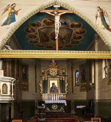 Zdjęcie nr 1: Kościół pomocniczny pw. Wniebowzięcia Najświętszej Marii Panny w Woli Radziszowskiej to niewielkich rozmiarów, orientowana, jednonawowa budowla drewniana, konstrukcji zrębowej, z wieżą w słup. Prezbiterium jest zamknięte wielobocznie, nieco wyższa i szersza nawa ma rzut prostokąta zbliżonego do kwadratu. Do prezbiterium od strony północnej przylega zakrystia, od wschodniej Ogrójec, przy nawie od południa umieszczona została niewielka, prostokątna kruchta. Od zachodu do budowli dostawiona jest czworoboczna wieża o pochyłych ścianach, z podwieszoną izbicą z czworobocznymi występami na przekątnikach; hełm ostrosłupowy z czterema wieżyczkami na występach. W przyziemiu wieży znajduje się kruchta, a dookoła wieży szalowane soboty. Wewnątrz świątyni stropy; w nawie z zaskrzynieniami. Otwór tęczowy ma kształt ostrołuku, belka jest profilowana, na niej umieszczony jest krucyfiks o charakterze późnogotyckim. Chór muzyczny w zachodniej części nawy jest drewniany, wsparty na dwóch kolumnach. Okna nawy i prezbiterium są głównie prostokątne zamknięte półkoliście; z witrażami (z wyjątkiem okna za ołtarzem głównym); ponadto budowlę doświetlają niewielkie okienka prostokątne. Do świątyni prowadzi dwoje drzwi ostrołukowych, trzecie od strony zachodniej przerobiono w 1933 roku. Dachy kościoła są kryte gontem, ponad nawą i kruchtą południową dwuspadowe, nad zakrystią jednospadowy, nad prezbiterium wielopołaciowy. Wieżyczka na sygnaturkę o formach barokowych z glorietą, cebulastym hełmem zwieńczonym kulą oraz krzyżem; kryta blachą. Świątynia usytuowana jest na niewielkiej działce, wydzielonej ogrodzeniem z drewnianych bali, krytym gontem. Bramy wiodące na posesję umieszczono od zachodu oraz w południowo-wschodnim narożniku działki.