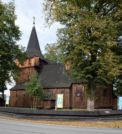 Zdjęcie nr 3: Kościół pomocniczny pw. Wniebowzięcia Najświętszej Marii Panny w Woli Radziszowskiej to niewielkich rozmiarów, orientowana, jednonawowa budowla drewniana, konstrukcji zrębowej, z wieżą w słup. Prezbiterium jest zamknięte wielobocznie, nieco wyższa i szersza nawa ma rzut prostokąta zbliżonego do kwadratu. Do prezbiterium od strony północnej przylega zakrystia, od wschodniej Ogrójec, przy nawie od południa umieszczona została niewielka, prostokątna kruchta. Od zachodu do budowli dostawiona jest czworoboczna wieża o pochyłych ścianach, z podwieszoną izbicą z czworobocznymi występami na przekątnikach; hełm ostrosłupowy z czterema wieżyczkami na występach. W przyziemiu wieży znajduje się kruchta, a dookoła wieży szalowane soboty. Wewnątrz świątyni stropy; w nawie z zaskrzynieniami. Otwór tęczowy ma kształt ostrołuku, belka jest profilowana, na niej umieszczony jest krucyfiks o charakterze późnogotyckim. Chór muzyczny w zachodniej części nawy jest drewniany, wsparty na dwóch kolumnach. Okna nawy i prezbiterium są głównie prostokątne zamknięte półkoliście; z witrażami (z wyjątkiem okna za ołtarzem głównym); ponadto budowlę doświetlają niewielkie okienka prostokątne. Do świątyni prowadzi dwoje drzwi ostrołukowych, trzecie od strony zachodniej przerobiono w 1933 roku. Dachy kościoła są kryte gontem, ponad nawą i kruchtą południową dwuspadowe, nad zakrystią jednospadowy, nad prezbiterium wielopołaciowy. Wieżyczka na sygnaturkę o formach barokowych z glorietą, cebulastym hełmem zwieńczonym kulą oraz krzyżem; kryta blachą. Świątynia usytuowana jest na niewielkiej działce, wydzielonej ogrodzeniem z drewnianych bali, krytym gontem. Bramy wiodące na posesję umieszczono od zachodu oraz w południowo-wschodnim narożniku działki.