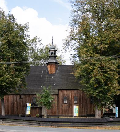 Zdjęcie nr 5: Kościół pomocniczny pw. Wniebowzięcia Najświętszej Marii Panny w Woli Radziszowskiej to niewielkich rozmiarów, orientowana, jednonawowa budowla drewniana, konstrukcji zrębowej, z wieżą w słup. Prezbiterium jest zamknięte wielobocznie, nieco wyższa i szersza nawa ma rzut prostokąta zbliżonego do kwadratu. Do prezbiterium od strony północnej przylega zakrystia, od wschodniej Ogrójec, przy nawie od południa umieszczona została niewielka, prostokątna kruchta. Od zachodu do budowli dostawiona jest czworoboczna wieża o pochyłych ścianach, z podwieszoną izbicą z czworobocznymi występami na przekątnikach; hełm ostrosłupowy z czterema wieżyczkami na występach. W przyziemiu wieży znajduje się kruchta, a dookoła wieży szalowane soboty. Wewnątrz świątyni stropy; w nawie z zaskrzynieniami. Otwór tęczowy ma kształt ostrołuku, belka jest profilowana, na niej umieszczony jest krucyfiks o charakterze późnogotyckim. Chór muzyczny w zachodniej części nawy jest drewniany, wsparty na dwóch kolumnach. Okna nawy i prezbiterium są głównie prostokątne zamknięte półkoliście; z witrażami (z wyjątkiem okna za ołtarzem głównym); ponadto budowlę doświetlają niewielkie okienka prostokątne. Do świątyni prowadzi dwoje drzwi ostrołukowych, trzecie od strony zachodniej przerobiono w 1933 roku. Dachy kościoła są kryte gontem, ponad nawą i kruchtą południową dwuspadowe, nad zakrystią jednospadowy, nad prezbiterium wielopołaciowy. Wieżyczka na sygnaturkę o formach barokowych z glorietą, cebulastym hełmem zwieńczonym kulą oraz krzyżem; kryta blachą. Świątynia usytuowana jest na niewielkiej działce, wydzielonej ogrodzeniem z drewnianych bali, krytym gontem. Bramy wiodące na posesję umieszczono od zachodu oraz w południowo-wschodnim narożniku działki.