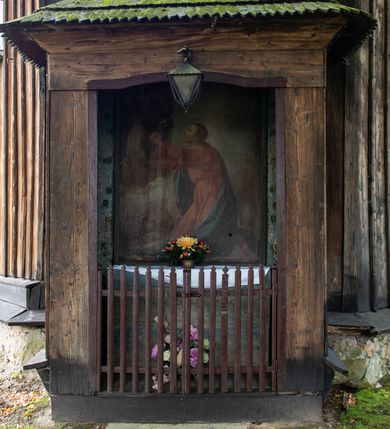 Zdjęcie nr 22: Kościół pomocniczny pw. Wniebowzięcia Najświętszej Marii Panny w Woli Radziszowskiej to niewielkich rozmiarów, orientowana, jednonawowa budowla drewniana, konstrukcji zrębowej, z wieżą w słup. Prezbiterium jest zamknięte wielobocznie, nieco wyższa i szersza nawa ma rzut prostokąta zbliżonego do kwadratu. Do prezbiterium od strony północnej przylega zakrystia, od wschodniej Ogrójec, przy nawie od południa umieszczona została niewielka, prostokątna kruchta. Od zachodu do budowli dostawiona jest czworoboczna wieża o pochyłych ścianach, z podwieszoną izbicą z czworobocznymi występami na przekątnikach; hełm ostrosłupowy z czterema wieżyczkami na występach. W przyziemiu wieży znajduje się kruchta, a dookoła wieży szalowane soboty. Wewnątrz świątyni stropy; w nawie z zaskrzynieniami. Otwór tęczowy ma kształt ostrołuku, belka jest profilowana, na niej umieszczony jest krucyfiks o charakterze późnogotyckim. Chór muzyczny w zachodniej części nawy jest drewniany, wsparty na dwóch kolumnach. Okna nawy i prezbiterium są głównie prostokątne zamknięte półkoliście; z witrażami (z wyjątkiem okna za ołtarzem głównym); ponadto budowlę doświetlają niewielkie okienka prostokątne. Do świątyni prowadzi dwoje drzwi ostrołukowych, trzecie od strony zachodniej przerobiono w 1933 roku. Dachy kościoła są kryte gontem, ponad nawą i kruchtą południową dwuspadowe, nad zakrystią jednospadowy, nad prezbiterium wielopołaciowy. Wieżyczka na sygnaturkę o formach barokowych z glorietą, cebulastym hełmem zwieńczonym kulą oraz krzyżem; kryta blachą. Świątynia usytuowana jest na niewielkiej działce, wydzielonej ogrodzeniem z drewnianych bali, krytym gontem. Bramy wiodące na posesję umieszczono od zachodu oraz w południowo-wschodnim narożniku działki.