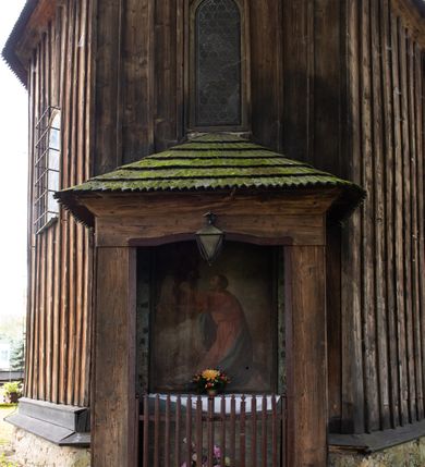 Zdjęcie nr 25: Kościół pomocniczny pw. Wniebowzięcia Najświętszej Marii Panny w Woli Radziszowskiej to niewielkich rozmiarów, orientowana, jednonawowa budowla drewniana, konstrukcji zrębowej, z wieżą w słup. Prezbiterium jest zamknięte wielobocznie, nieco wyższa i szersza nawa ma rzut prostokąta zbliżonego do kwadratu. Do prezbiterium od strony północnej przylega zakrystia, od wschodniej Ogrójec, przy nawie od południa umieszczona została niewielka, prostokątna kruchta. Od zachodu do budowli dostawiona jest czworoboczna wieża o pochyłych ścianach, z podwieszoną izbicą z czworobocznymi występami na przekątnikach; hełm ostrosłupowy z czterema wieżyczkami na występach. W przyziemiu wieży znajduje się kruchta, a dookoła wieży szalowane soboty. Wewnątrz świątyni stropy; w nawie z zaskrzynieniami. Otwór tęczowy ma kształt ostrołuku, belka jest profilowana, na niej umieszczony jest krucyfiks o charakterze późnogotyckim. Chór muzyczny w zachodniej części nawy jest drewniany, wsparty na dwóch kolumnach. Okna nawy i prezbiterium są głównie prostokątne zamknięte półkoliście; z witrażami (z wyjątkiem okna za ołtarzem głównym); ponadto budowlę doświetlają niewielkie okienka prostokątne. Do świątyni prowadzi dwoje drzwi ostrołukowych, trzecie od strony zachodniej przerobiono w 1933 roku. Dachy kościoła są kryte gontem, ponad nawą i kruchtą południową dwuspadowe, nad zakrystią jednospadowy, nad prezbiterium wielopołaciowy. Wieżyczka na sygnaturkę o formach barokowych z glorietą, cebulastym hełmem zwieńczonym kulą oraz krzyżem; kryta blachą. Świątynia usytuowana jest na niewielkiej działce, wydzielonej ogrodzeniem z drewnianych bali, krytym gontem. Bramy wiodące na posesję umieszczono od zachodu oraz w południowo-wschodnim narożniku działki.