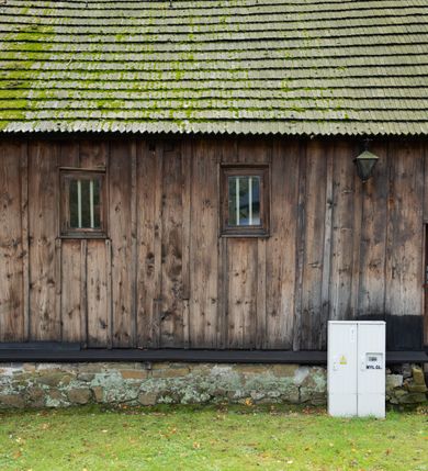 Zdjęcie nr 26: Kościół pomocniczny pw. Wniebowzięcia Najświętszej Marii Panny w Woli Radziszowskiej to niewielkich rozmiarów, orientowana, jednonawowa budowla drewniana, konstrukcji zrębowej, z wieżą w słup. Prezbiterium jest zamknięte wielobocznie, nieco wyższa i szersza nawa ma rzut prostokąta zbliżonego do kwadratu. Do prezbiterium od strony północnej przylega zakrystia, od wschodniej Ogrójec, przy nawie od południa umieszczona została niewielka, prostokątna kruchta. Od zachodu do budowli dostawiona jest czworoboczna wieża o pochyłych ścianach, z podwieszoną izbicą z czworobocznymi występami na przekątnikach; hełm ostrosłupowy z czterema wieżyczkami na występach. W przyziemiu wieży znajduje się kruchta, a dookoła wieży szalowane soboty. Wewnątrz świątyni stropy; w nawie z zaskrzynieniami. Otwór tęczowy ma kształt ostrołuku, belka jest profilowana, na niej umieszczony jest krucyfiks o charakterze późnogotyckim. Chór muzyczny w zachodniej części nawy jest drewniany, wsparty na dwóch kolumnach. Okna nawy i prezbiterium są głównie prostokątne zamknięte półkoliście; z witrażami (z wyjątkiem okna za ołtarzem głównym); ponadto budowlę doświetlają niewielkie okienka prostokątne. Do świątyni prowadzi dwoje drzwi ostrołukowych, trzecie od strony zachodniej przerobiono w 1933 roku. Dachy kościoła są kryte gontem, ponad nawą i kruchtą południową dwuspadowe, nad zakrystią jednospadowy, nad prezbiterium wielopołaciowy. Wieżyczka na sygnaturkę o formach barokowych z glorietą, cebulastym hełmem zwieńczonym kulą oraz krzyżem; kryta blachą. Świątynia usytuowana jest na niewielkiej działce, wydzielonej ogrodzeniem z drewnianych bali, krytym gontem. Bramy wiodące na posesję umieszczono od zachodu oraz w południowo-wschodnim narożniku działki.