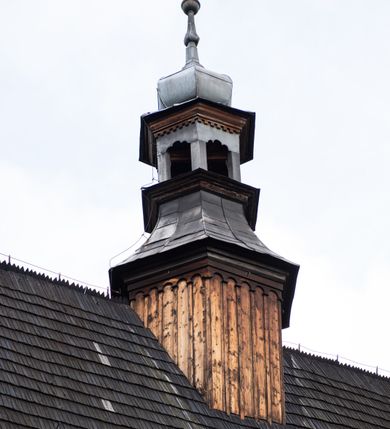 Zdjęcie nr 33: Kościół pomocniczny pw. Wniebowzięcia Najświętszej Marii Panny w Woli Radziszowskiej to niewielkich rozmiarów, orientowana, jednonawowa budowla drewniana, konstrukcji zrębowej, z wieżą w słup. Prezbiterium jest zamknięte wielobocznie, nieco wyższa i szersza nawa ma rzut prostokąta zbliżonego do kwadratu. Do prezbiterium od strony północnej przylega zakrystia, od wschodniej Ogrójec, przy nawie od południa umieszczona została niewielka, prostokątna kruchta. Od zachodu do budowli dostawiona jest czworoboczna wieża o pochyłych ścianach, z podwieszoną izbicą z czworobocznymi występami na przekątnikach; hełm ostrosłupowy z czterema wieżyczkami na występach. W przyziemiu wieży znajduje się kruchta, a dookoła wieży szalowane soboty. Wewnątrz świątyni stropy; w nawie z zaskrzynieniami. Otwór tęczowy ma kształt ostrołuku, belka jest profilowana, na niej umieszczony jest krucyfiks o charakterze późnogotyckim. Chór muzyczny w zachodniej części nawy jest drewniany, wsparty na dwóch kolumnach. Okna nawy i prezbiterium są głównie prostokątne zamknięte półkoliście; z witrażami (z wyjątkiem okna za ołtarzem głównym); ponadto budowlę doświetlają niewielkie okienka prostokątne. Do świątyni prowadzi dwoje drzwi ostrołukowych, trzecie od strony zachodniej przerobiono w 1933 roku. Dachy kościoła są kryte gontem, ponad nawą i kruchtą południową dwuspadowe, nad zakrystią jednospadowy, nad prezbiterium wielopołaciowy. Wieżyczka na sygnaturkę o formach barokowych z glorietą, cebulastym hełmem zwieńczonym kulą oraz krzyżem; kryta blachą. Świątynia usytuowana jest na niewielkiej działce, wydzielonej ogrodzeniem z drewnianych bali, krytym gontem. Bramy wiodące na posesję umieszczono od zachodu oraz w południowo-wschodnim narożniku działki.