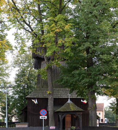 Zdjęcie nr 35: Kościół pomocniczny pw. Wniebowzięcia Najświętszej Marii Panny w Woli Radziszowskiej to niewielkich rozmiarów, orientowana, jednonawowa budowla drewniana, konstrukcji zrębowej, z wieżą w słup. Prezbiterium jest zamknięte wielobocznie, nieco wyższa i szersza nawa ma rzut prostokąta zbliżonego do kwadratu. Do prezbiterium od strony północnej przylega zakrystia, od wschodniej Ogrójec, przy nawie od południa umieszczona została niewielka, prostokątna kruchta. Od zachodu do budowli dostawiona jest czworoboczna wieża o pochyłych ścianach, z podwieszoną izbicą z czworobocznymi występami na przekątnikach; hełm ostrosłupowy z czterema wieżyczkami na występach. W przyziemiu wieży znajduje się kruchta, a dookoła wieży szalowane soboty. Wewnątrz świątyni stropy; w nawie z zaskrzynieniami. Otwór tęczowy ma kształt ostrołuku, belka jest profilowana, na niej umieszczony jest krucyfiks o charakterze późnogotyckim. Chór muzyczny w zachodniej części nawy jest drewniany, wsparty na dwóch kolumnach. Okna nawy i prezbiterium są głównie prostokątne zamknięte półkoliście; z witrażami (z wyjątkiem okna za ołtarzem głównym); ponadto budowlę doświetlają niewielkie okienka prostokątne. Do świątyni prowadzi dwoje drzwi ostrołukowych, trzecie od strony zachodniej przerobiono w 1933 roku. Dachy kościoła są kryte gontem, ponad nawą i kruchtą południową dwuspadowe, nad zakrystią jednospadowy, nad prezbiterium wielopołaciowy. Wieżyczka na sygnaturkę o formach barokowych z glorietą, cebulastym hełmem zwieńczonym kulą oraz krzyżem; kryta blachą. Świątynia usytuowana jest na niewielkiej działce, wydzielonej ogrodzeniem z drewnianych bali, krytym gontem. Bramy wiodące na posesję umieszczono od zachodu oraz w południowo-wschodnim narożniku działki.