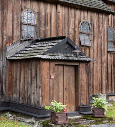 Zdjęcie nr 37: Kościół pomocniczny pw. Wniebowzięcia Najświętszej Marii Panny w Woli Radziszowskiej to niewielkich rozmiarów, orientowana, jednonawowa budowla drewniana, konstrukcji zrębowej, z wieżą w słup. Prezbiterium jest zamknięte wielobocznie, nieco wyższa i szersza nawa ma rzut prostokąta zbliżonego do kwadratu. Do prezbiterium od strony północnej przylega zakrystia, od wschodniej Ogrójec, przy nawie od południa umieszczona została niewielka, prostokątna kruchta. Od zachodu do budowli dostawiona jest czworoboczna wieża o pochyłych ścianach, z podwieszoną izbicą z czworobocznymi występami na przekątnikach; hełm ostrosłupowy z czterema wieżyczkami na występach. W przyziemiu wieży znajduje się kruchta, a dookoła wieży szalowane soboty. Wewnątrz świątyni stropy; w nawie z zaskrzynieniami. Otwór tęczowy ma kształt ostrołuku, belka jest profilowana, na niej umieszczony jest krucyfiks o charakterze późnogotyckim. Chór muzyczny w zachodniej części nawy jest drewniany, wsparty na dwóch kolumnach. Okna nawy i prezbiterium są głównie prostokątne zamknięte półkoliście; z witrażami (z wyjątkiem okna za ołtarzem głównym); ponadto budowlę doświetlają niewielkie okienka prostokątne. Do świątyni prowadzi dwoje drzwi ostrołukowych, trzecie od strony zachodniej przerobiono w 1933 roku. Dachy kościoła są kryte gontem, ponad nawą i kruchtą południową dwuspadowe, nad zakrystią jednospadowy, nad prezbiterium wielopołaciowy. Wieżyczka na sygnaturkę o formach barokowych z glorietą, cebulastym hełmem zwieńczonym kulą oraz krzyżem; kryta blachą. Świątynia usytuowana jest na niewielkiej działce, wydzielonej ogrodzeniem z drewnianych bali, krytym gontem. Bramy wiodące na posesję umieszczono od zachodu oraz w południowo-wschodnim narożniku działki.