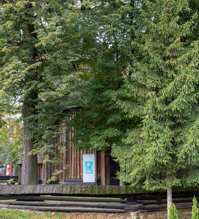 Zdjęcie nr 46: Kościół pomocniczny pw. Wniebowzięcia Najświętszej Marii Panny w Woli Radziszowskiej to niewielkich rozmiarów, orientowana, jednonawowa budowla drewniana, konstrukcji zrębowej, z wieżą w słup. Prezbiterium jest zamknięte wielobocznie, nieco wyższa i szersza nawa ma rzut prostokąta zbliżonego do kwadratu. Do prezbiterium od strony północnej przylega zakrystia, od wschodniej Ogrójec, przy nawie od południa umieszczona została niewielka, prostokątna kruchta. Od zachodu do budowli dostawiona jest czworoboczna wieża o pochyłych ścianach, z podwieszoną izbicą z czworobocznymi występami na przekątnikach; hełm ostrosłupowy z czterema wieżyczkami na występach. W przyziemiu wieży znajduje się kruchta, a dookoła wieży szalowane soboty. Wewnątrz świątyni stropy; w nawie z zaskrzynieniami. Otwór tęczowy ma kształt ostrołuku, belka jest profilowana, na niej umieszczony jest krucyfiks o charakterze późnogotyckim. Chór muzyczny w zachodniej części nawy jest drewniany, wsparty na dwóch kolumnach. Okna nawy i prezbiterium są głównie prostokątne zamknięte półkoliście; z witrażami (z wyjątkiem okna za ołtarzem głównym); ponadto budowlę doświetlają niewielkie okienka prostokątne. Do świątyni prowadzi dwoje drzwi ostrołukowych, trzecie od strony zachodniej przerobiono w 1933 roku. Dachy kościoła są kryte gontem, ponad nawą i kruchtą południową dwuspadowe, nad zakrystią jednospadowy, nad prezbiterium wielopołaciowy. Wieżyczka na sygnaturkę o formach barokowych z glorietą, cebulastym hełmem zwieńczonym kulą oraz krzyżem; kryta blachą. Świątynia usytuowana jest na niewielkiej działce, wydzielonej ogrodzeniem z drewnianych bali, krytym gontem. Bramy wiodące na posesję umieszczono od zachodu oraz w południowo-wschodnim narożniku działki.