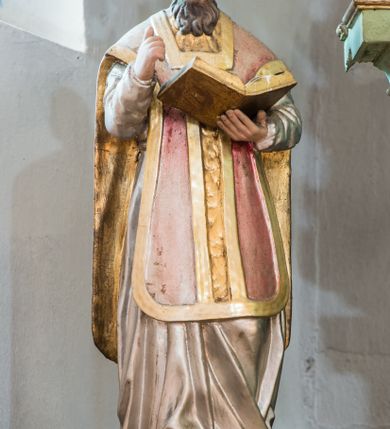 Zdjęcie nr 1: Figura niemal pełnoplastyczna, z tyłu ścięta i drążona ukazuje świętego, przedstawionego w pozycji stojącej, w kontrapoście. Święty w lewej dłoni trzyma otwartą księgę, a prawą wznosi ugiętą. Ma pociągłą twarz, duże oczy, nos długi o prostym profilu i lekko rozchylone usta. Twarz ma okoloną brązowymi włosami formowanymi w pukle i długą brodą. Jest ubrany w srebrną albę i ornat w kolorze różowym ze złotą kolumną i lamowaniem. Polichromia w partiach ciała naturalistyczna.