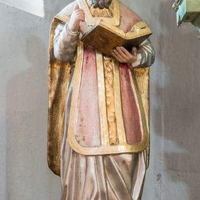 Zdjęcie nr 1: Figura niemal pełnoplastyczna, z tyłu ścięta i drążona ukazuje świętego, przedstawionego w pozycji stojącej, w kontrapoście. Święty w lewej dłoni trzyma otwartą księgę, a prawą wznosi ugiętą. Ma pociągłą twarz, duże oczy, nos długi o prostym profilu i lekko rozchylone usta. Twarz ma okoloną brązowymi włosami formowanymi w pukle i długą brodą. Jest ubrany w srebrną albę i ornat w kolorze różowym ze złotą kolumną i lamowaniem. Polichromia w partiach ciała naturalistyczna.