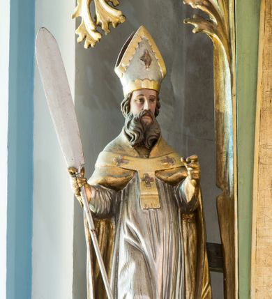 Zdjęcie nr 1: Figura niemal pełnoplastyczna, z tyłu ścięta i drążona. Święty Wojciech został ukazany w pozycji stojącej z uniesionymi rękami, w prawej dłoni trzymając wiosło. Twarz ma pociągłą, brwi uniesione, oczy szeroko otwarte, nos prosty, brodę długą, dzielącą się w dwa pukle. Jest ubrany w jasnoróżową sutannę, srebrną komżę oraz złotą kapę i paliusz. Na głowie ma infułę, na dłoniach rękawiczki. Polichromia w partiach ciała naturalistyczna. 