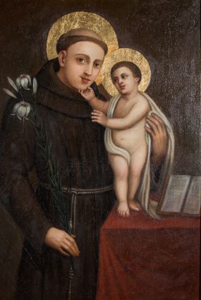 Zdjęcie nr 1: Obraz w kształcie stojącego prostokąta z przedstawieniem św. Antoniego Padewskiego z Dzieciątkiem. Święty został ukazany w ujęciu do kolan, zwrócony w lewo, w stronę Dzieciątka stojącego na blacie przykrytym czerwonym obrusem. Głowa świętego jest delikatnie przechylona w lewo, lewa ręka obejmuje Dzieciątko, prawa opuszczona trzyma kwiat lilii. Święty ma owalną twarz o młodzieńczych rysach, na głowie tonsurę. Jest ubrany w habit franciszkański. Dzieciątko ukazane zostało niemal nagie, z białą chustą okrywającą biodro i przerzuconą przez prawe ramię. Prawą ręką Chrystus dotyka brody świętego, lewą wyciąga w jego stronę. U stóp Dzieciątka leży otwarta księga. Wokół głów postaci złote nimby. Tło kompozycji jednolite, ciemnobrązowe. Na odwrocie napis malowany farbą „Fundator Walenty / Tekiela. / 1840. / 24 lipca”.