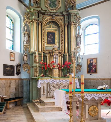 Zdjęcie nr 2: Ołtarz przyścienny, architektoniczny, jednoosiowy, dwukondygnacyjny ze zwieńczeniem. Mensa prostopadłościenna z kamiennym blatem z portatylem, boki mensy z polerowanych płyt kamiennych. Dekoracja antepedium współczesna z aplikowanych metalowych motywów kielicha z hostią i kłosów. Retabulum ujęte parą kolumn korynckich ustawionych na schodkowych cokołach podzielonych gzymsem na dwie strefy. Podpory wspierają belkowanie przerwane w partii architrawu i fryzu nad polem środkowym. Belkowanie zamknięte wydatnym, profilowanym, wyłamanym gzymsem. Powyżej, na osiach zewnętrznych kolumn ustawione odcinki falistego przyczółka o wolutowo skręconych końcach. W polu środkowym wnęka w kształcie stojącego prostokąta zamknięta łukiem półkolistym, na kluczu łuku rzeźba gołębicy Ducha Świętego. Wewnątrz prostokątny otwór na obraz – wymiennie przedstawienie św. Marii Magdaleny pod krzyżem, „Noli me tangere” oraz wizerunek Marki Boskiej Myślenickiej. Zwieńczenie ujęte parą pilastrów, zamknięte trójbocznie z ośmiobocznym polem środkowym. Wnęka pola środkowego retabulum i zwieńczenia ujęta szeroką, ażurową ramą formowaną z wolutowo skręconych liści akantu. W zwieńczeniu obraz przedstawiający Boga Ojca. Ściany cokołów dekorowane płycinami wypełnionymi skręconymi liśćmi akantu. Poniżej gzymsu zamykającego retabulum ażurowy ornament akantowy. U góry boki nastawy ujęte ażurowymi uszakami formowanymi ze skręconych liści akantu, poniżej tworzących parę konsolek. Zwieńczenie ujęte uszakami formowanymi z ornamentu małżowinowo-chrząstowego. Na gzymsie zwieńczenia rzeźbione wazony i czworoliść z monogramem IHS na tle glorii promienistej. Na konsolkach po bokach retabulum ustawione figury św. Wojciecha i świętego z księgą po lewej oraz św. Stanisława i świętego z pastorałem po prawej stronie. Na odcinkach przyczółka figury uskrzydlonych aniołów. Całość struktury retabulum malowana w kolorze jasnozielonym. Detal architektoniczny, profilowania i ornamentyka złocone. 