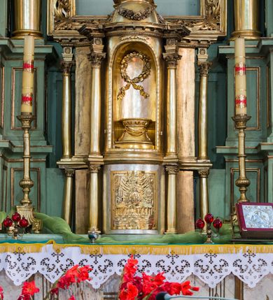 Zdjęcie nr 16: Ołtarz przyścienny, architektoniczny, jednoosiowy, dwukondygnacyjny ze zwieńczeniem. Mensa prostopadłościenna z kamiennym blatem z portatylem, boki mensy z polerowanych płyt kamiennych. Dekoracja antepedium współczesna z aplikowanych metalowych motywów kielicha z hostią i kłosów. Retabulum ujęte parą kolumn korynckich ustawionych na schodkowych cokołach podzielonych gzymsem na dwie strefy. Podpory wspierają belkowanie przerwane w partii architrawu i fryzu nad polem środkowym. Belkowanie zamknięte wydatnym, profilowanym, wyłamanym gzymsem. Powyżej, na osiach zewnętrznych kolumn ustawione odcinki falistego przyczółka o wolutowo skręconych końcach. W polu środkowym wnęka w kształcie stojącego prostokąta zamknięta łukiem półkolistym, na kluczu łuku rzeźba gołębicy Ducha Świętego. Wewnątrz prostokątny otwór na obraz – wymiennie przedstawienie św. Marii Magdaleny pod krzyżem, „Noli me tangere” oraz wizerunek Marki Boskiej Myślenickiej. Zwieńczenie ujęte parą pilastrów, zamknięte trójbocznie z ośmiobocznym polem środkowym. Wnęka pola środkowego retabulum i zwieńczenia ujęta szeroką, ażurową ramą formowaną z wolutowo skręconych liści akantu. W zwieńczeniu obraz przedstawiający Boga Ojca. Ściany cokołów dekorowane płycinami wypełnionymi skręconymi liśćmi akantu. Poniżej gzymsu zamykającego retabulum ażurowy ornament akantowy. U góry boki nastawy ujęte ażurowymi uszakami formowanymi ze skręconych liści akantu, poniżej tworzących parę konsolek. Zwieńczenie ujęte uszakami formowanymi z ornamentu małżowinowo-chrząstowego. Na gzymsie zwieńczenia rzeźbione wazony i czworoliść z monogramem IHS na tle glorii promienistej. Na konsolkach po bokach retabulum ustawione figury św. Wojciecha i świętego z księgą po lewej oraz św. Stanisława i świętego z pastorałem po prawej stronie. Na odcinkach przyczółka figury uskrzydlonych aniołów. Całość struktury retabulum malowana w kolorze jasnozielonym. Detal architektoniczny, profilowania i ornamentyka złocone. 