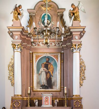 Zdjęcie nr 1: Ołtarz przyścienny, architektoniczny, na cokole. Mensa w typie sarkofagowym; antepedium dekorowane romboidalną plakietą z rozetą na tle liści. Na mensie tabernakulum na rzucie zbliżonym do kwadratu o ściętych przednich narożach, na profilowanej podstawie. Na froncie drzwi w kształcie stojącego prostokąta zamkniętego łukiem półkolistym dekorowane kielichem z hostią; na skośnych ściankach prostokątne płyciny. Zwieńczenie w formie gzymsu. Obok tabernakulum stoją niewielkie, całopostaciowe figurki aniołów – po lewej stronie skłaniającego się w modlitwie, po prawej wyciągającego ręce przed siebie. Nastawa ołtarzowa jednoosiowa, jednokondygnacyjna ze zwieńczeniem. Oś środkowa jest flankowana parą kolumn o kapitelach kompozytowych, ustawionych przed licem ołtarza, na tle zwielokrotnionych pilastrów. Cokoły kolumn dekorowane wieńcami laurowymi. Podpory dźwigają pełne, wyłamane wielokrotnie belkowanie oraz odpowiadające ich ułożeniu cokoły, na których klęczy para modlących się aniołów; na środku, na fryzie belkowania wić roślinna. W polu głównym, we wnęce w kształcie stojącego prostokąta obraz w kształcie takiegoż prostokąta zamkniętego łukiem półkolistym z przedstawieniem św. Józefa z małym Jezusem ujętego ramą z dekoracją w przyłuczach. 
Kondygnację ujmują ażurowe uszaki utworzone z suchej wici akantowej połączonej z rozwiniętymi kwiatkami. Zwieńczenie o kształcie wklęsło-wypukłym, zamknięte od góry łukiem nadwieszonym utworzonym z wolut spiętych płomienistym rocaille’em. Wypełnia je mały owalny obraz z przedstawieniem św. Maksymiliana Kolbe w profilowanej ramie. Spływy zwieńczenia dekorują liście palmowe. 
Struktura polichromowana na kolor jasnobrązowy ze złoconą i srebrzoną ornamentyką oraz detalami architektonicznymi; kolumny białe; tabernakulum białe z różowymi płycinami i złoconymi detalami. 
